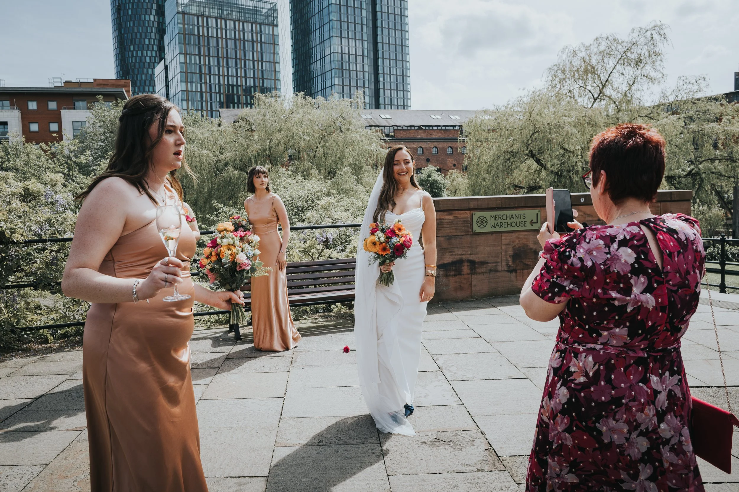 Bride has her photo taken by guest as bridesmaids watch. 