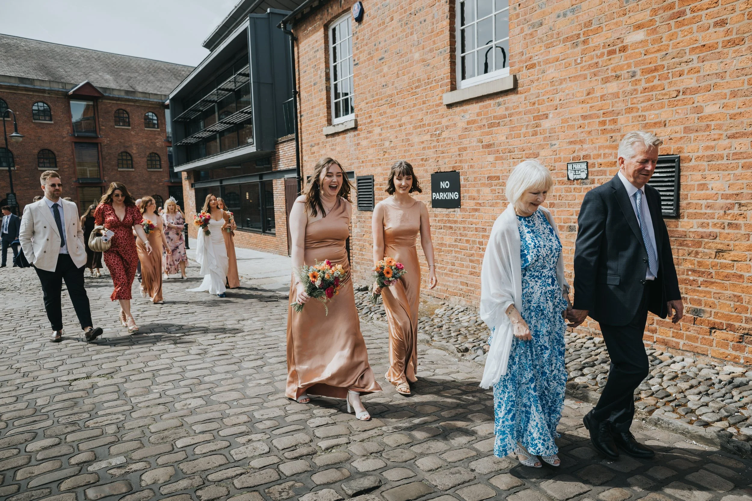 Guests walking on cobbled street on a sunny wedding day in Manchester. 
