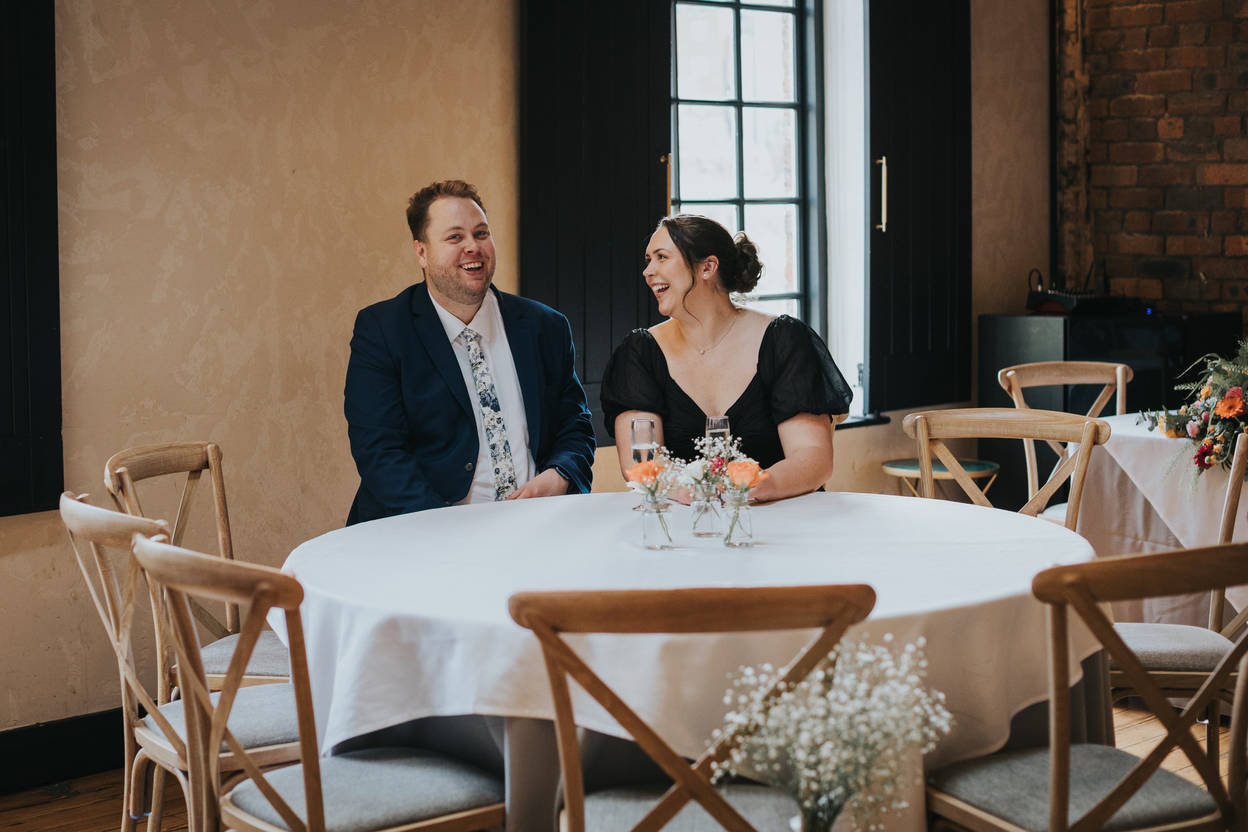 Wedding guests laugh at table. 