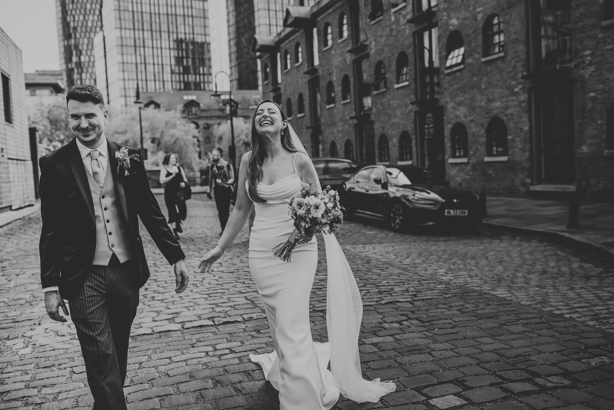 Black and white photo of Bride and Groom laughing on a cobbled street. 