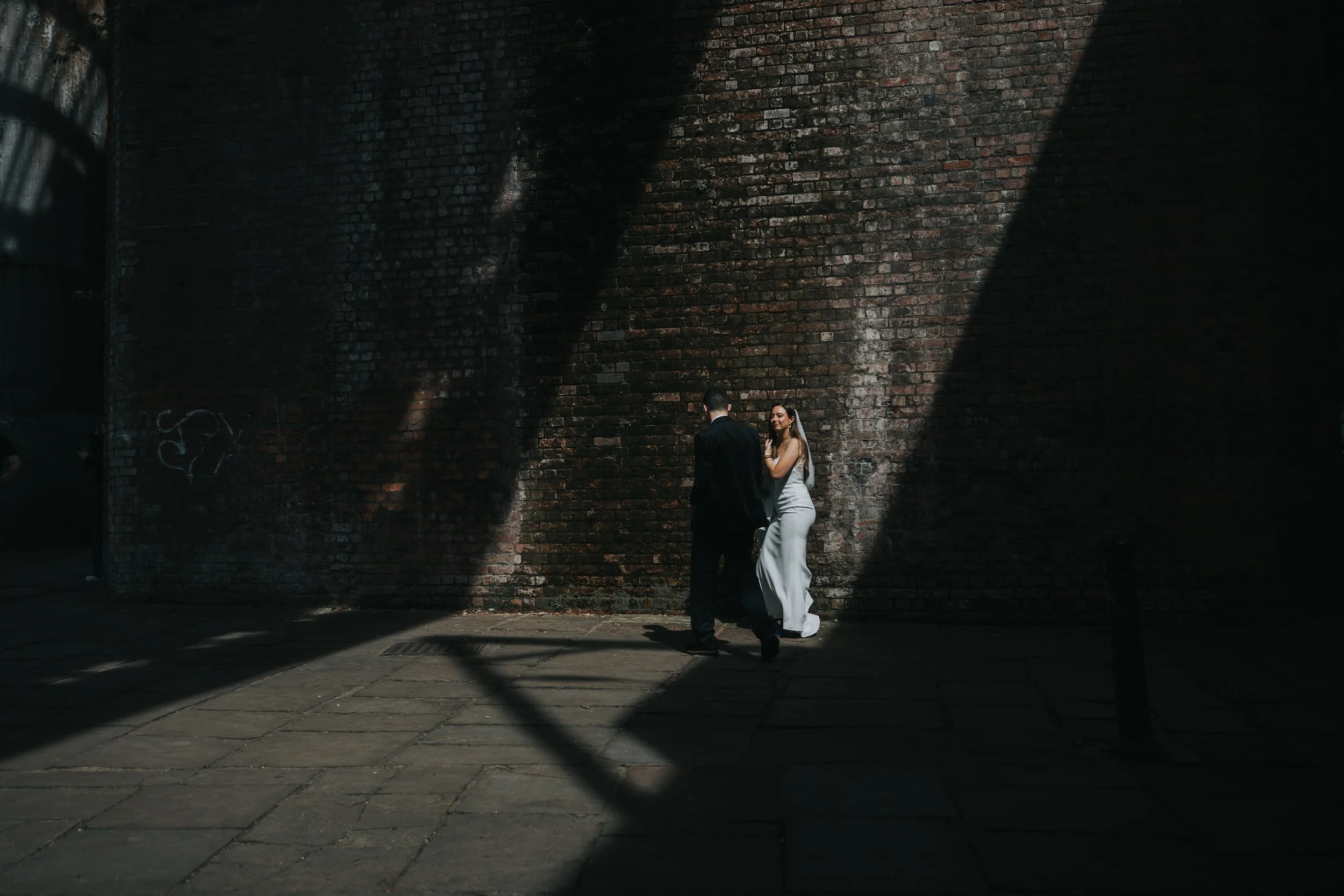 Bride and Groom walk under bridge into shard of light. 
