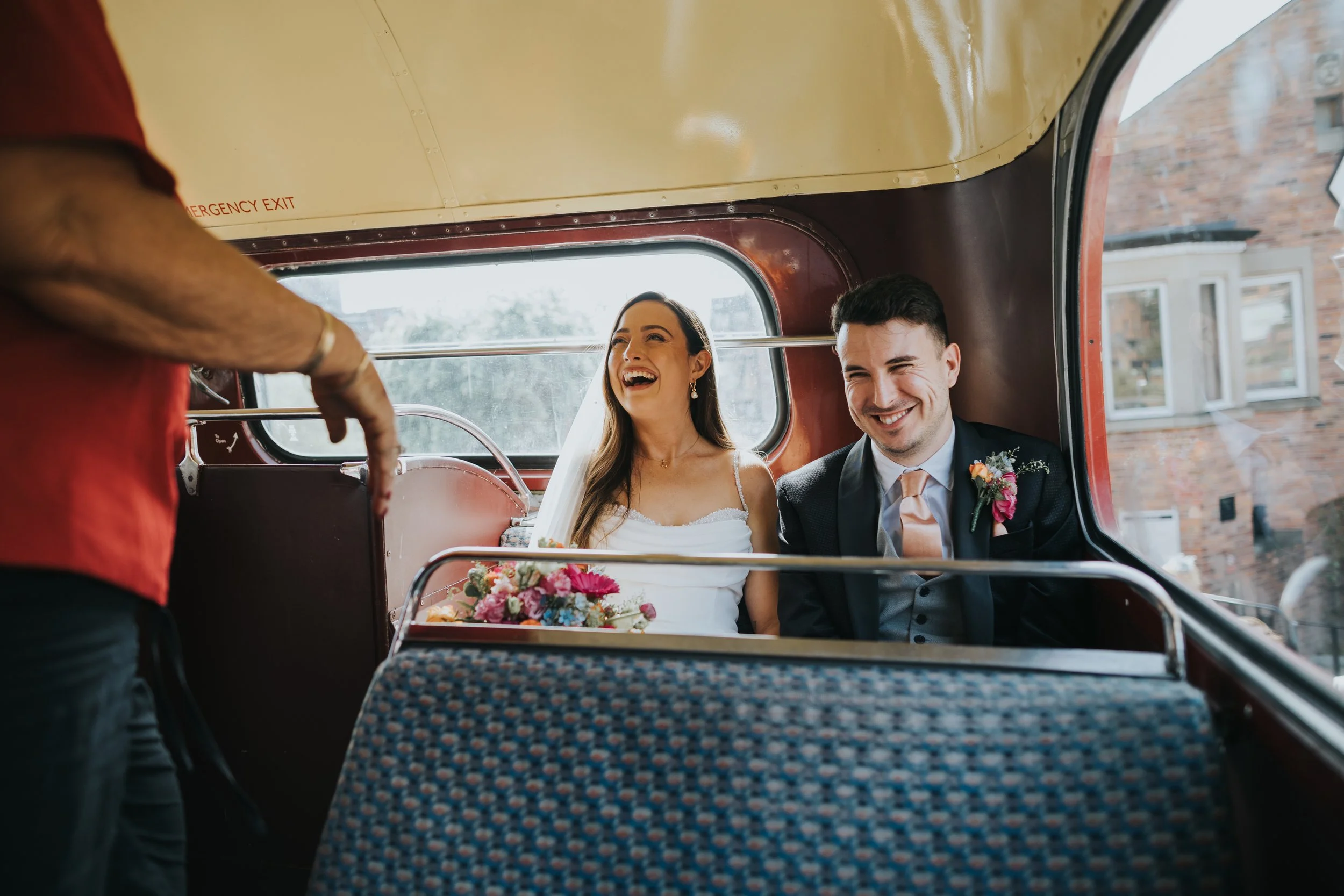 Bride and Groom laughing on back seat of wedding bus. 