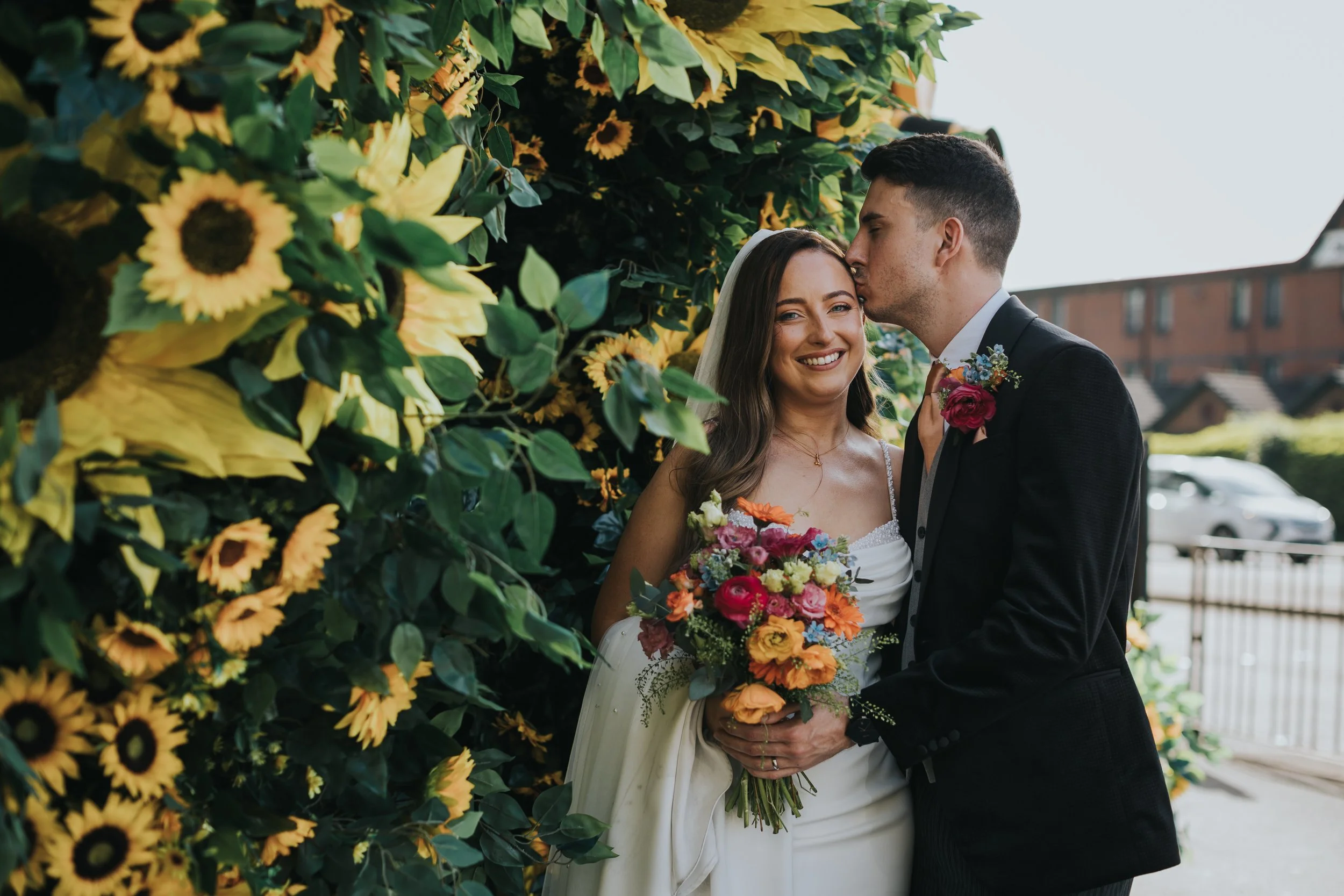 Bride and Groom kiss in front of sunflowers.