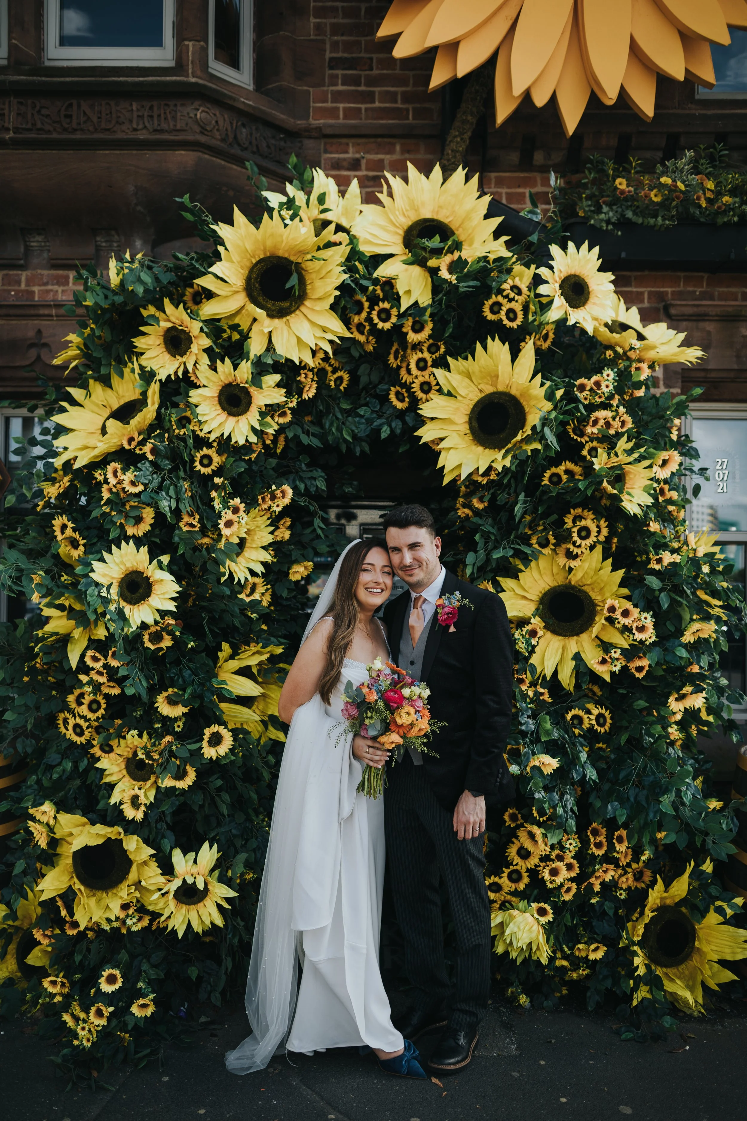 Bride and Groom in front of archway of Flowers outside Black Friars pub. 