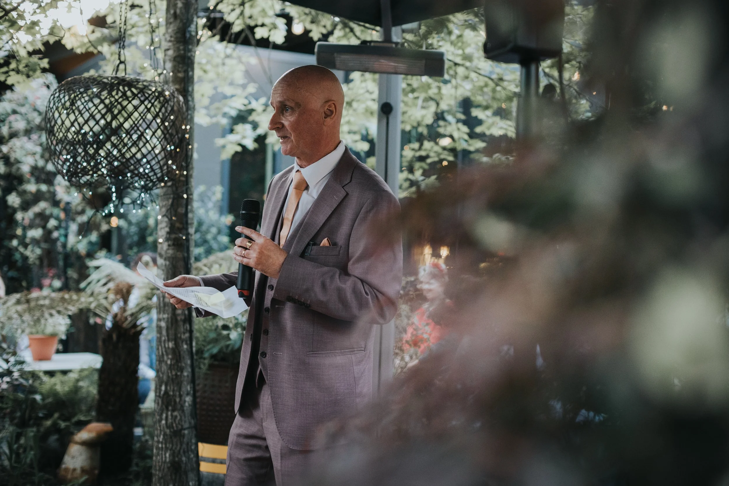 Father of the bride gives speech in leafy city jungle garden. 
