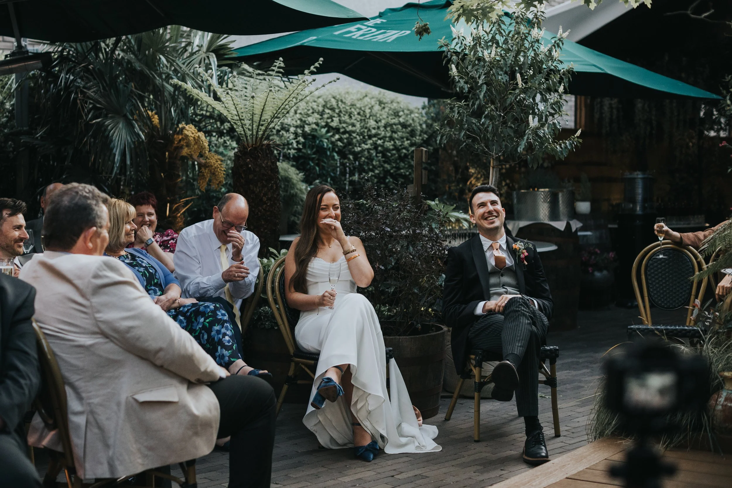 Bride and Groom laughing in garden as they listen to the speeches. 