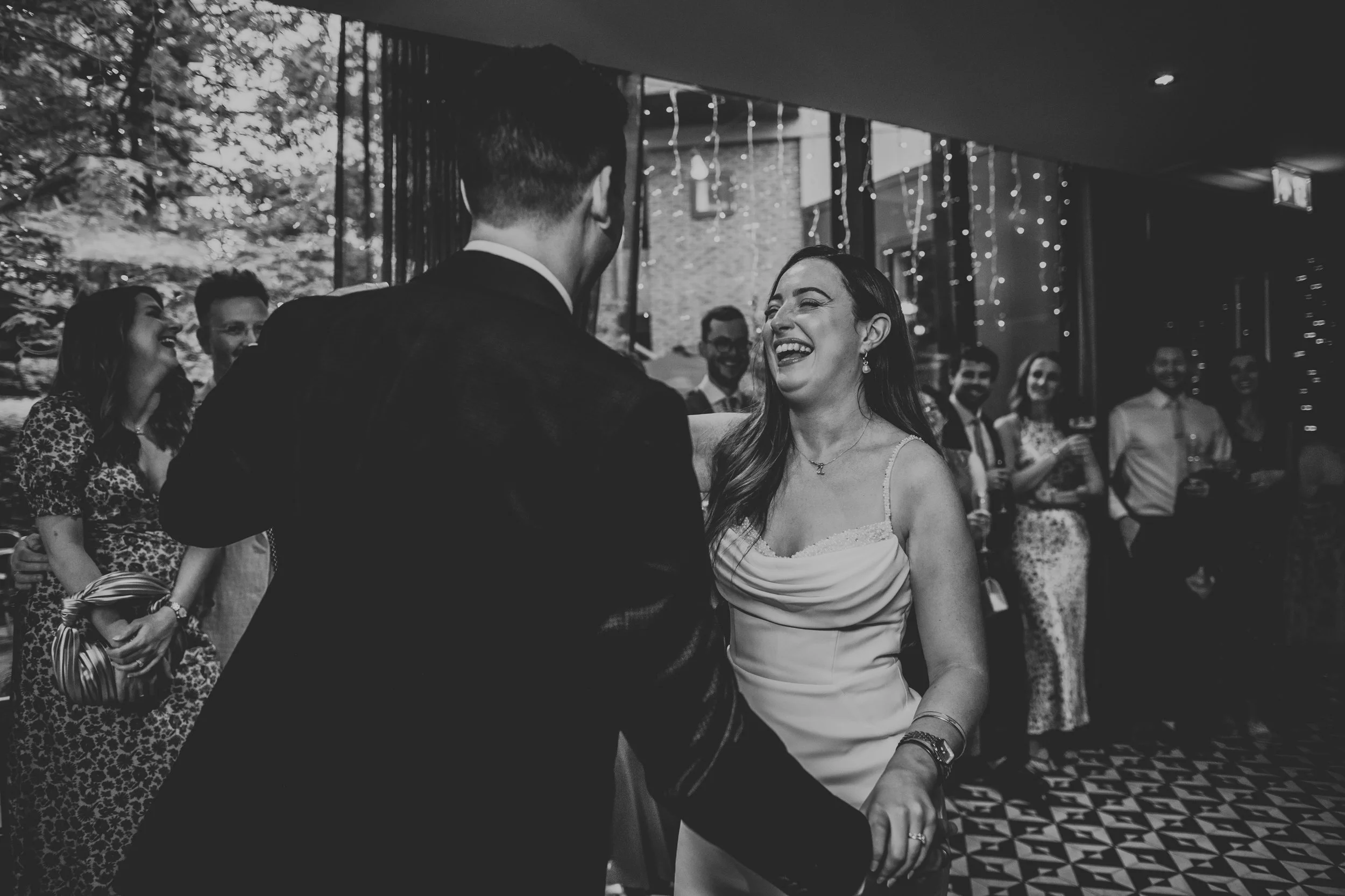 Bride laughs with groom on dance floor photo in black and white. 