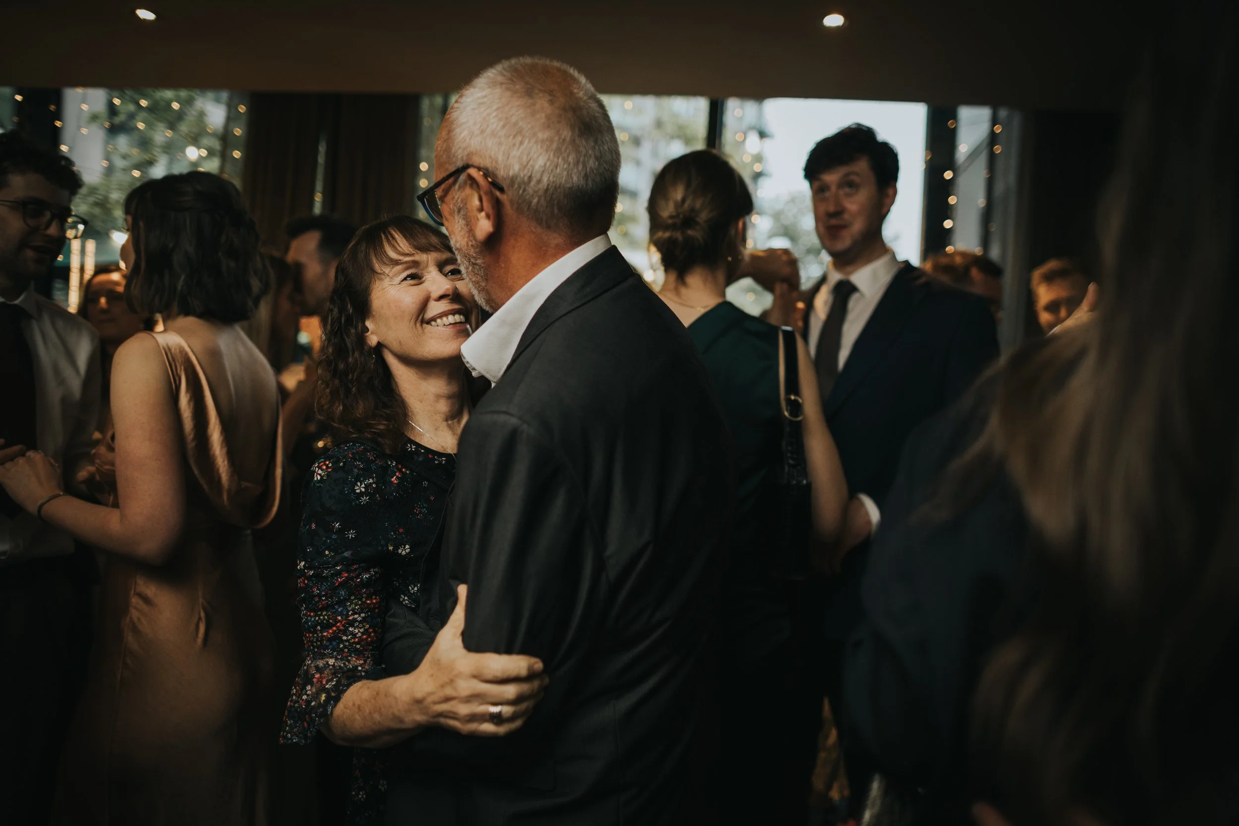 Wedding guests look at one and other lovingly on dance floor. 