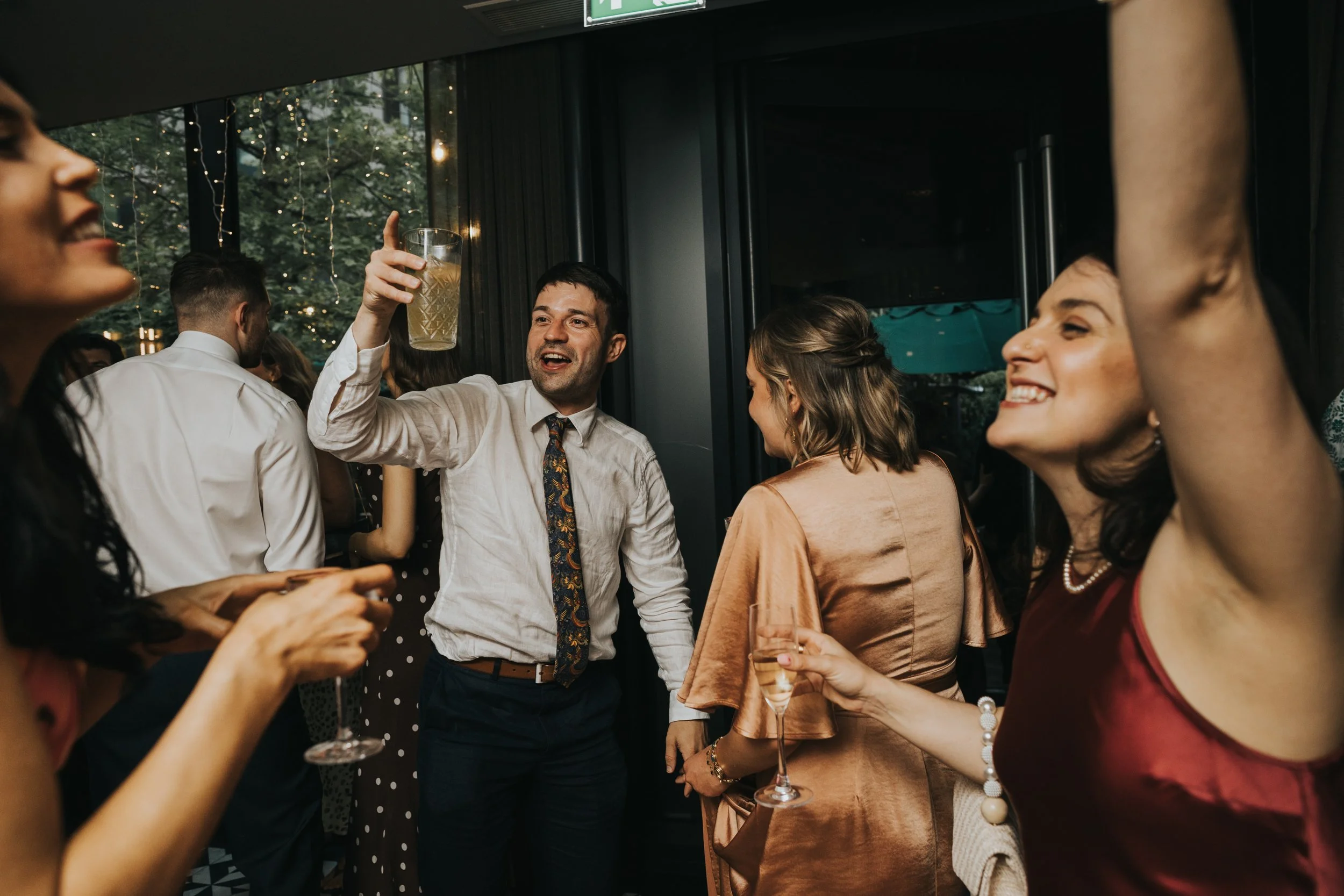 Guests hold drinks up and sing and dance. 