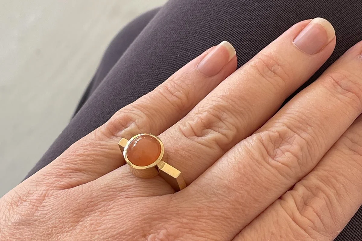 Orange moonstone cabochon bezel set in yellow gold on a chunky flat topped U shaped 9ct ring in wear