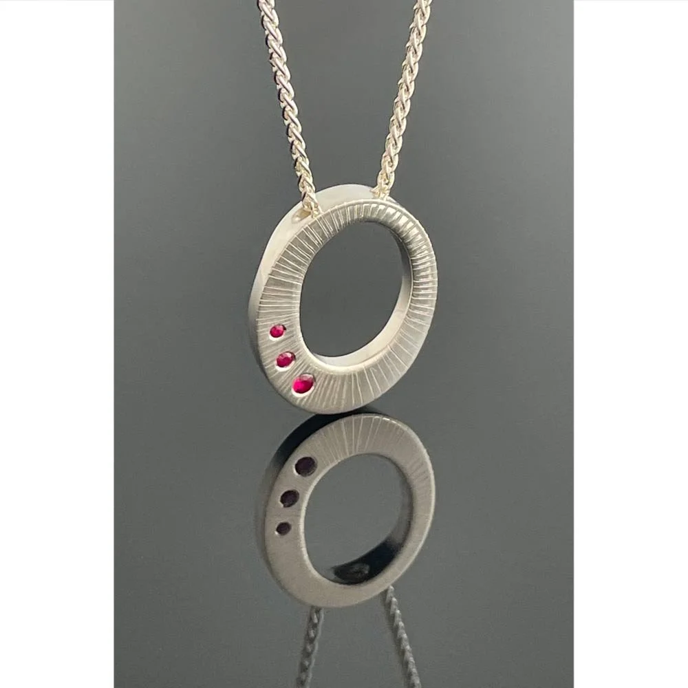 Oval silver pendant with three punch set rubies on a silver spiga chain