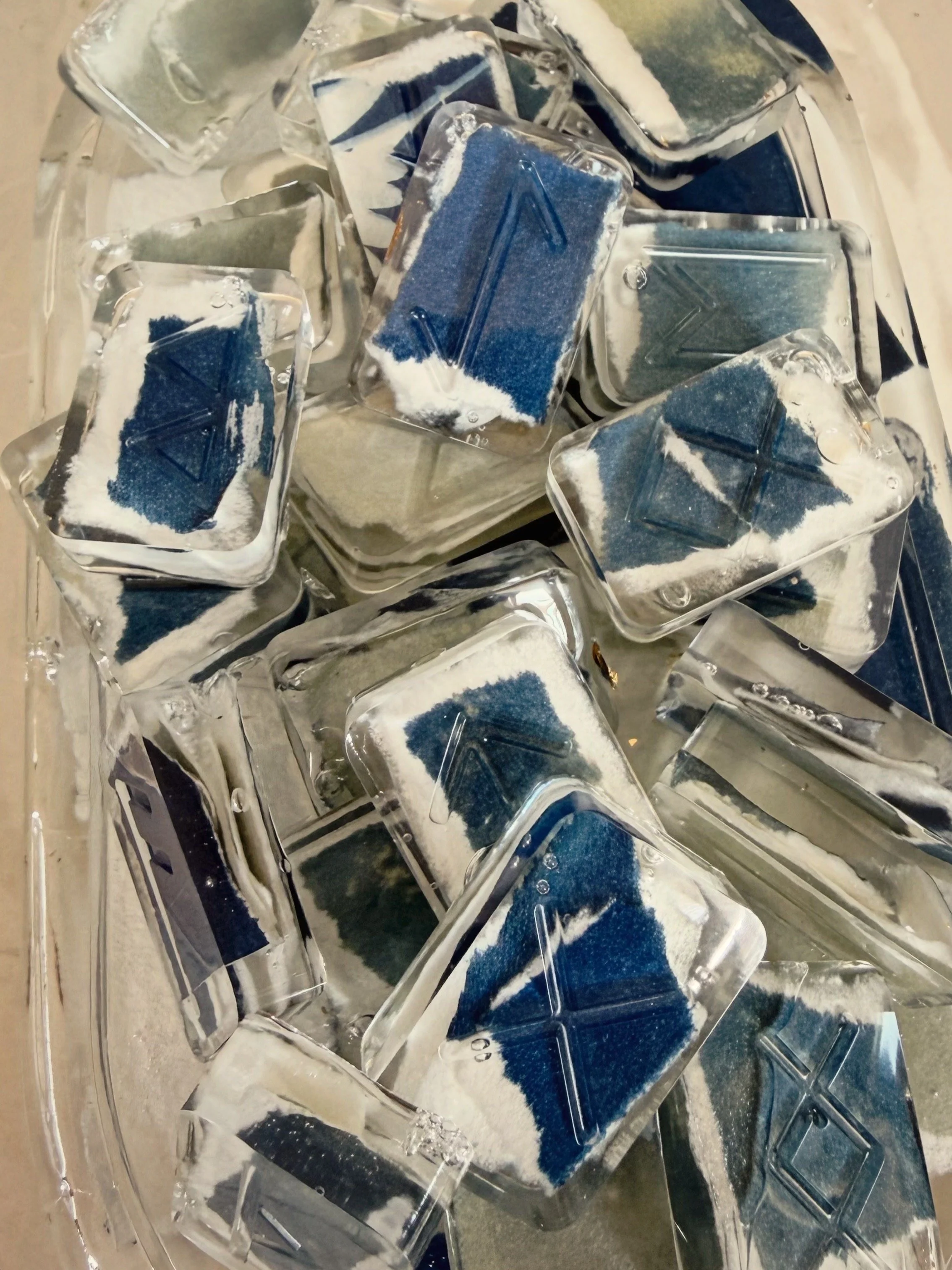 A close-up view of several ice cubes with a logo or symbol embedded in some of them, placed in a clear container.