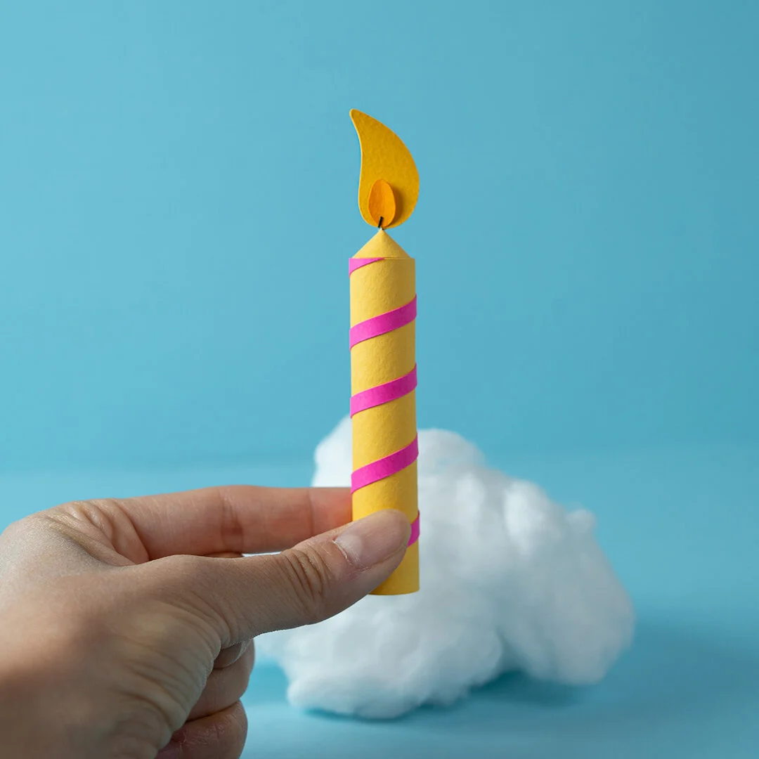A hand holds up a yellow paper candle. Behind the scenes image of animation.