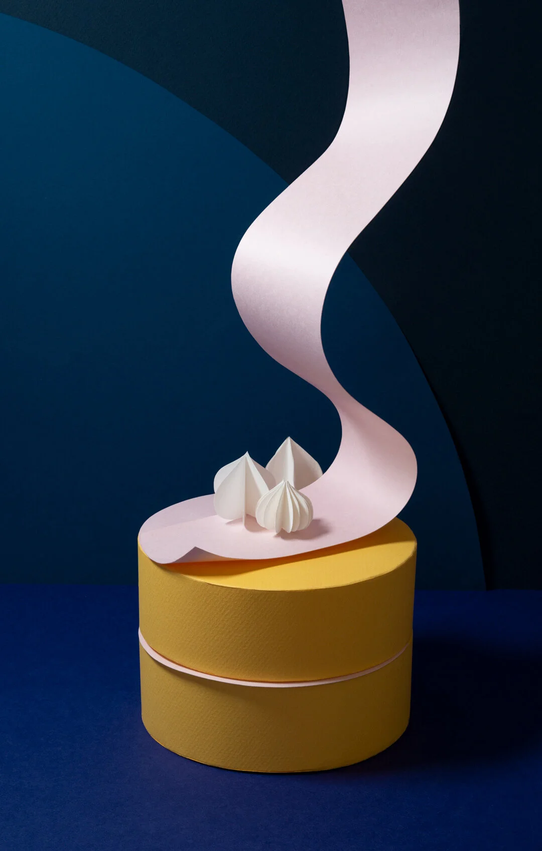 Yellow paper cake with light pink icing flowing down onto it from above. Set on a dark blue background.