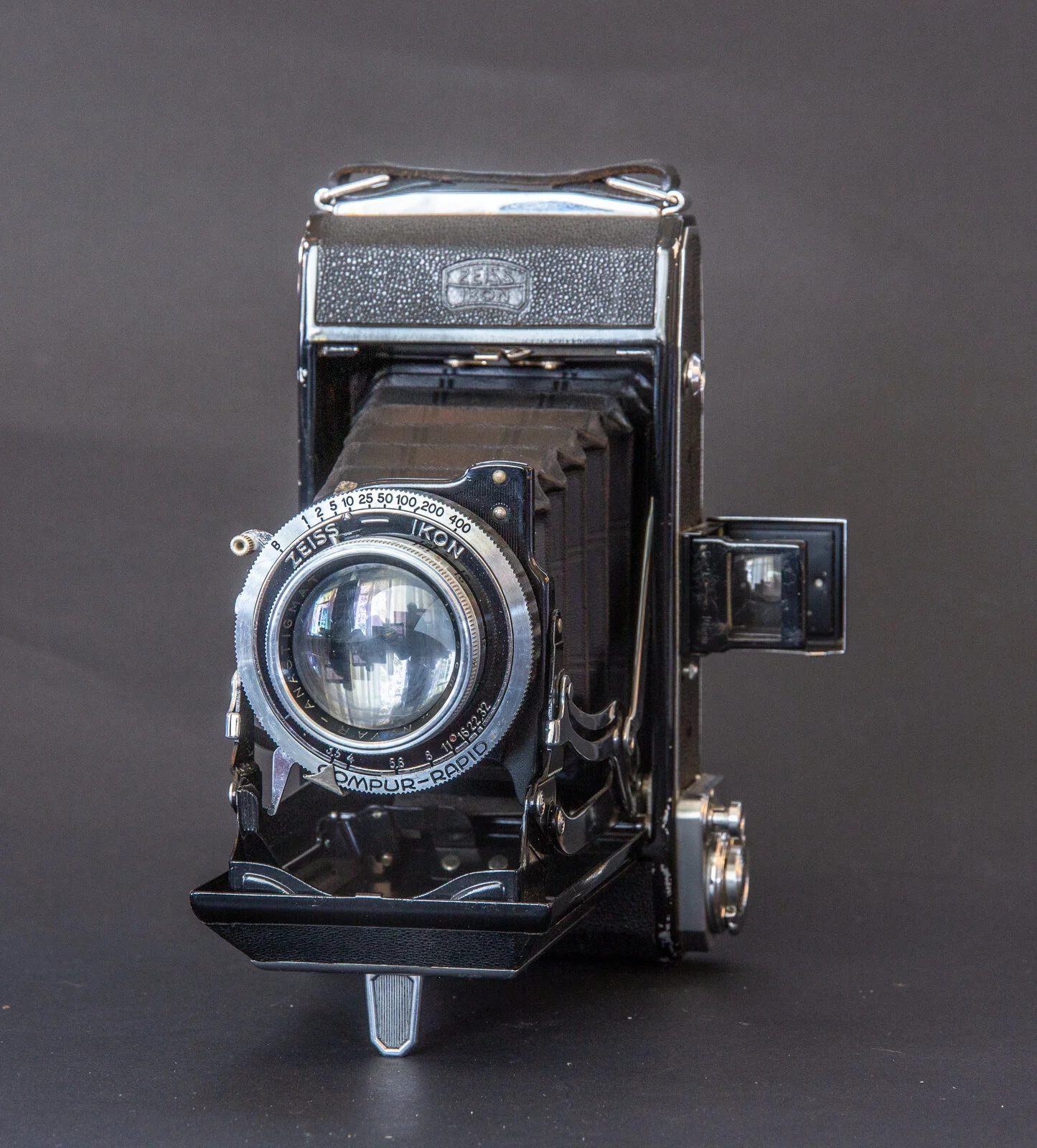 Caméra rétro sans miroir en noir avec objectif grand angle, réglages à baïonnette, et flash intégré, positionnée sur une surface noire.