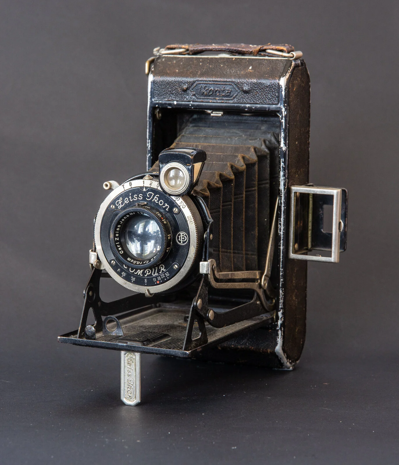Ancienne caméra photographique en métal noir avec objectif et mécanisme fragile, devant un fond noir