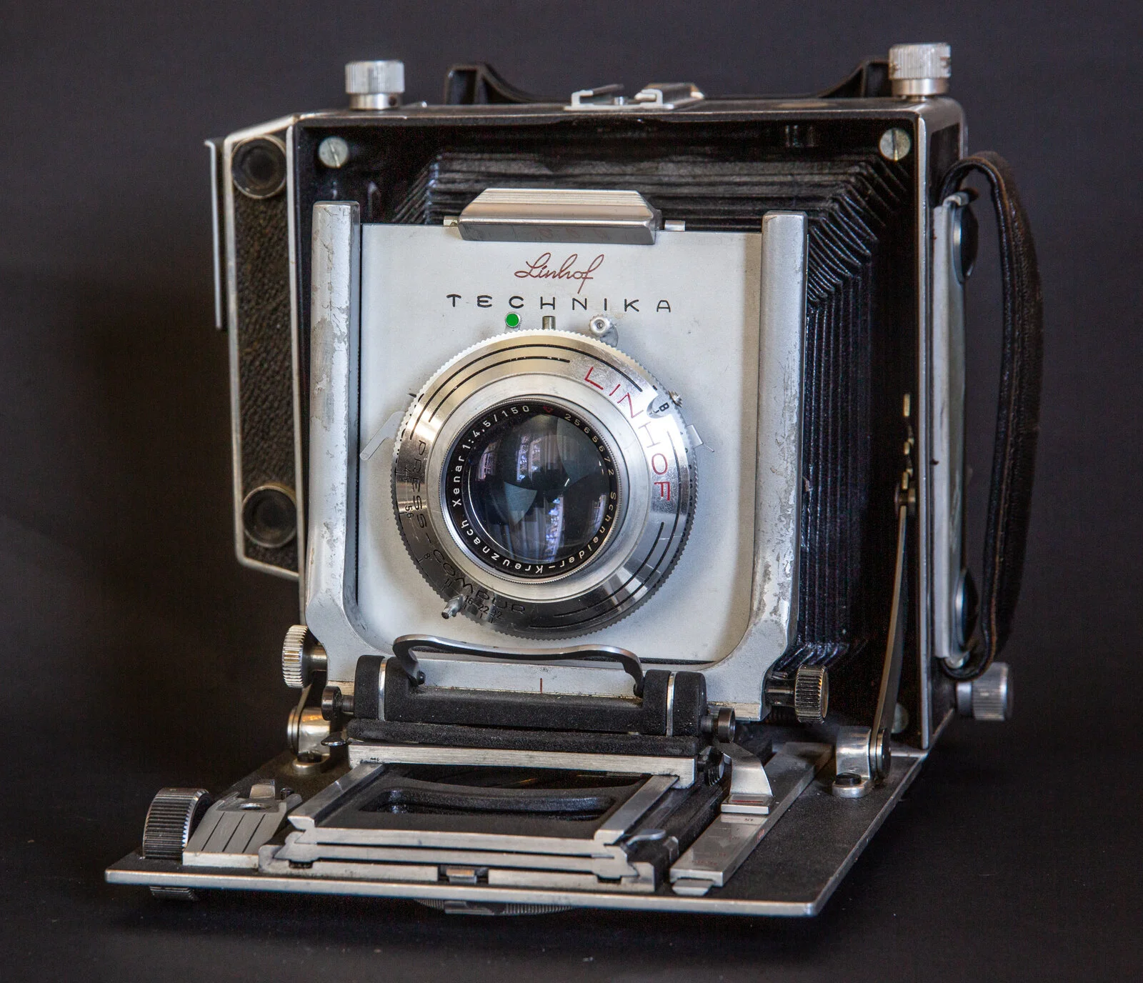 Appareil photo vintage avec objectif en métal, marqué 'Linhof' et 'Technika', posé sur une surface noire.