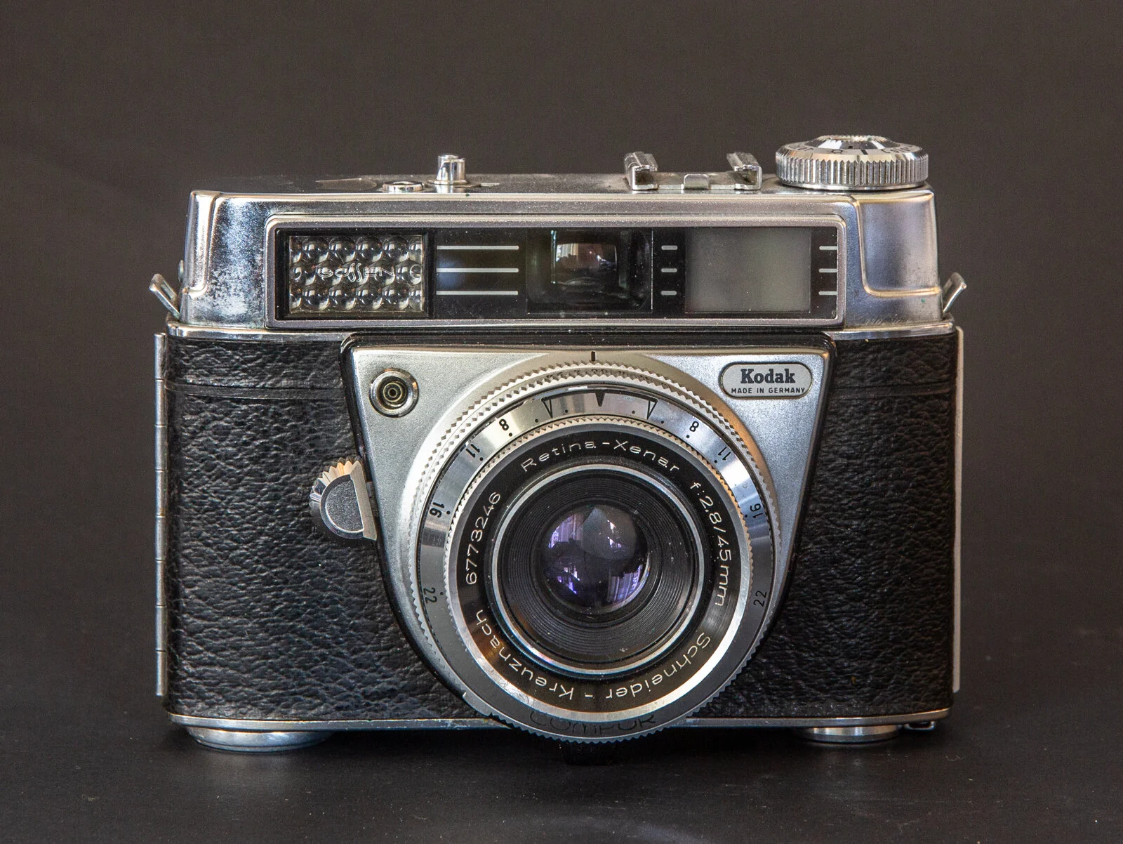 Appareil photo vintage en métal noir et argent, doté d'un objectif Schneider-Kreuznach sur un fond noir.