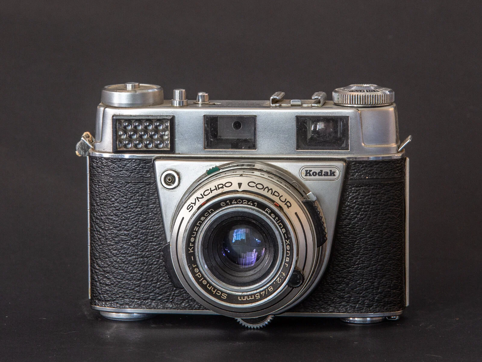 Appareil photo vintage Kodak avec lentille fixe et corps en métal et cuir noir, posé sur un fond noir.