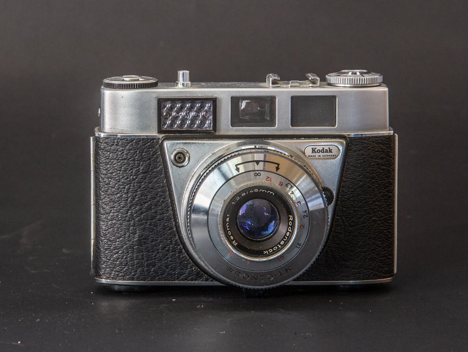 Appareil photo vintage Kodak avec boîtier en métal et lentille en métal, noir en cuir, contre fond noir.