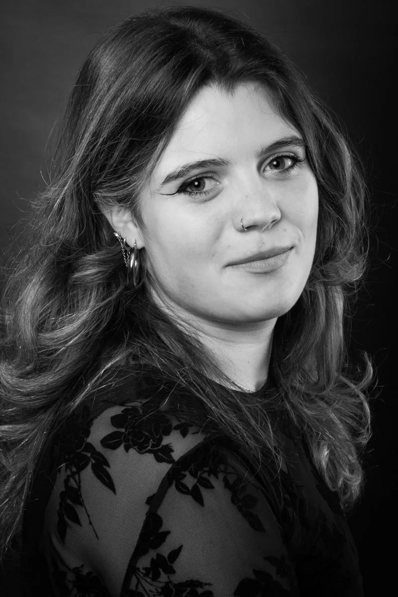 Portrait en noir et blanc d'une jeune femme avec des cheveux ondulés, portant des boucles d'oreilles et un vêtement à motif floral en dentelle.