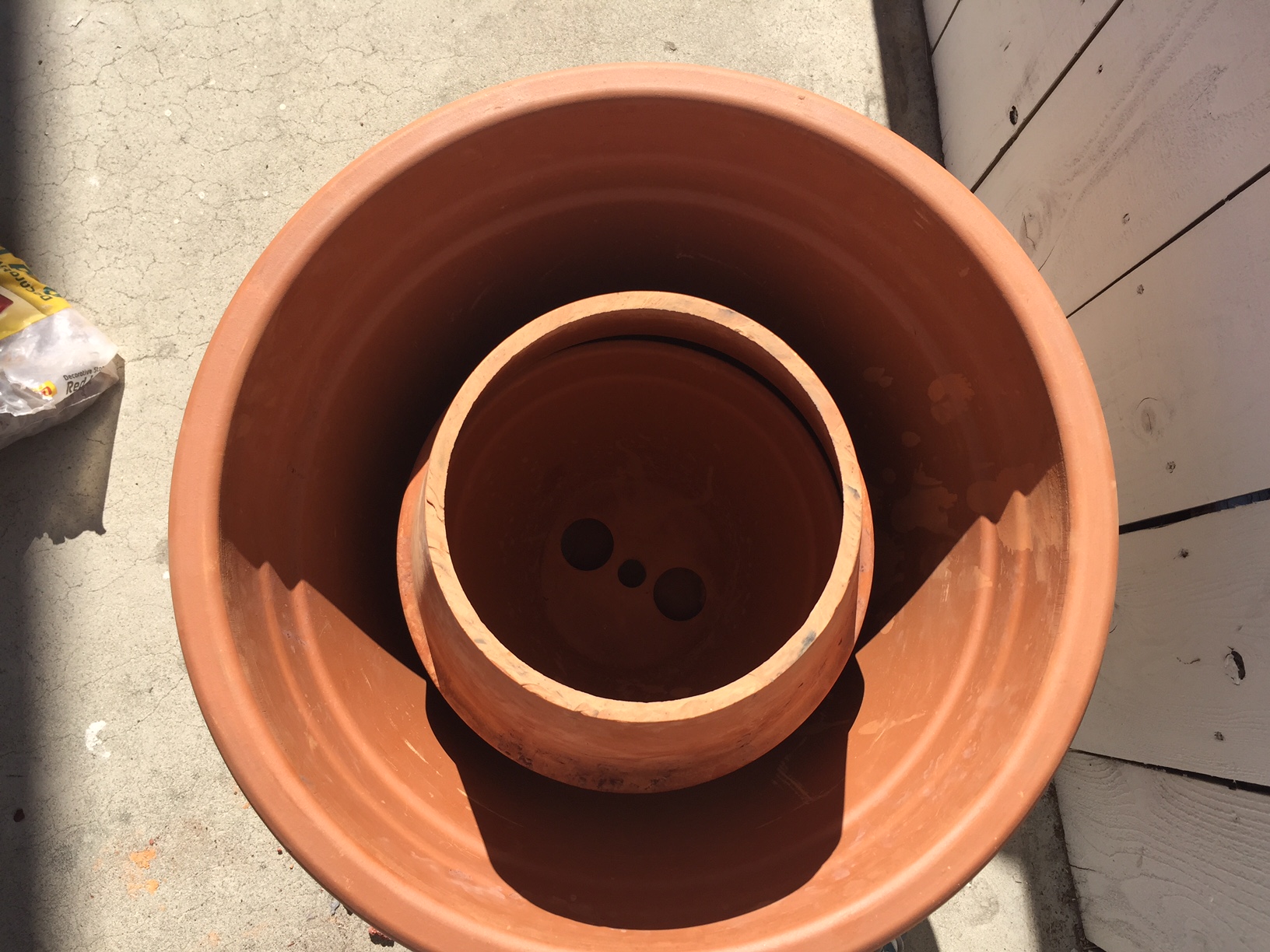  Invert the middle sized pot over the smallest one inside the largest, outer pot. This will create an interior cylinder. 