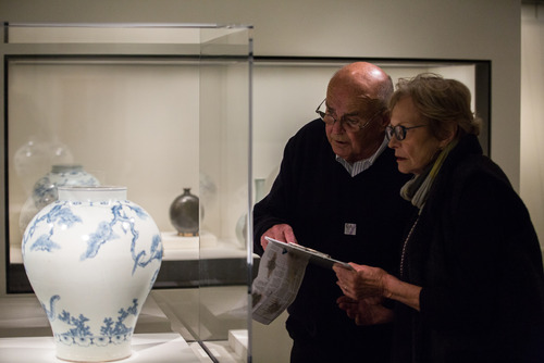 Museum visitors examine an 18th century Korean vase depicting a tiger smoking a long pipe, described by Miriam Mills, museum storyteller. May 2014.