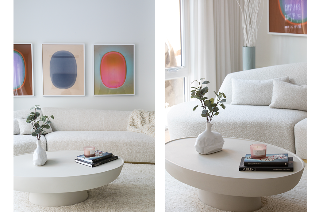 Modern living room with white boucle sofa, abstract wall art, round coffee table, vase with greenery, and a candle.