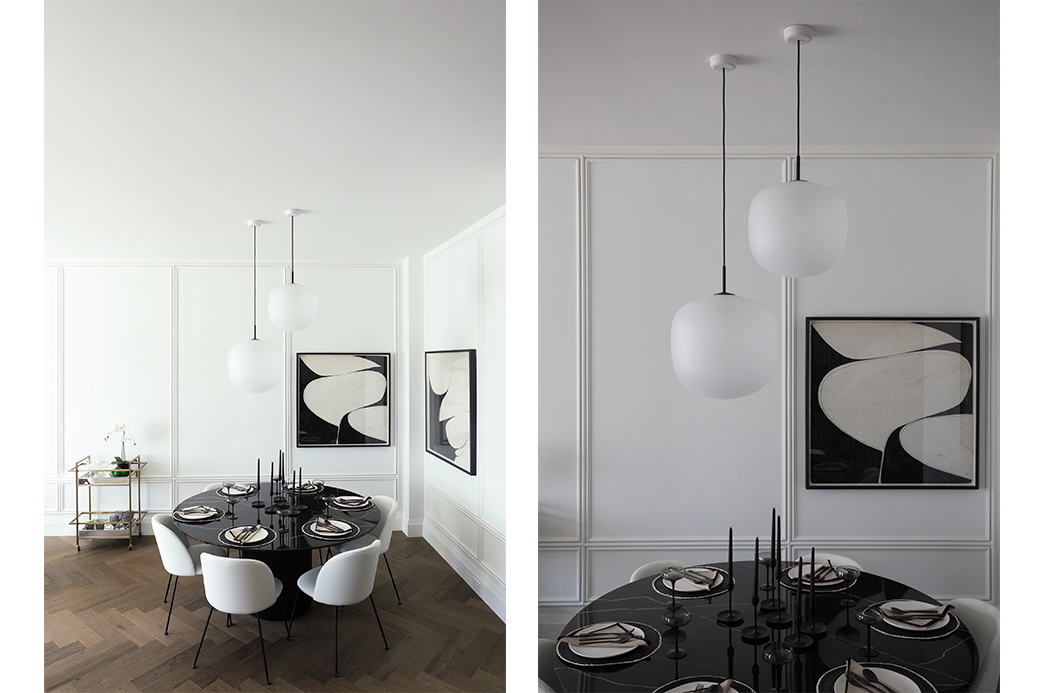 Modern dining room with round black table, white chairs, elegant light fixtures, abstract wall art, and wooden flooring.