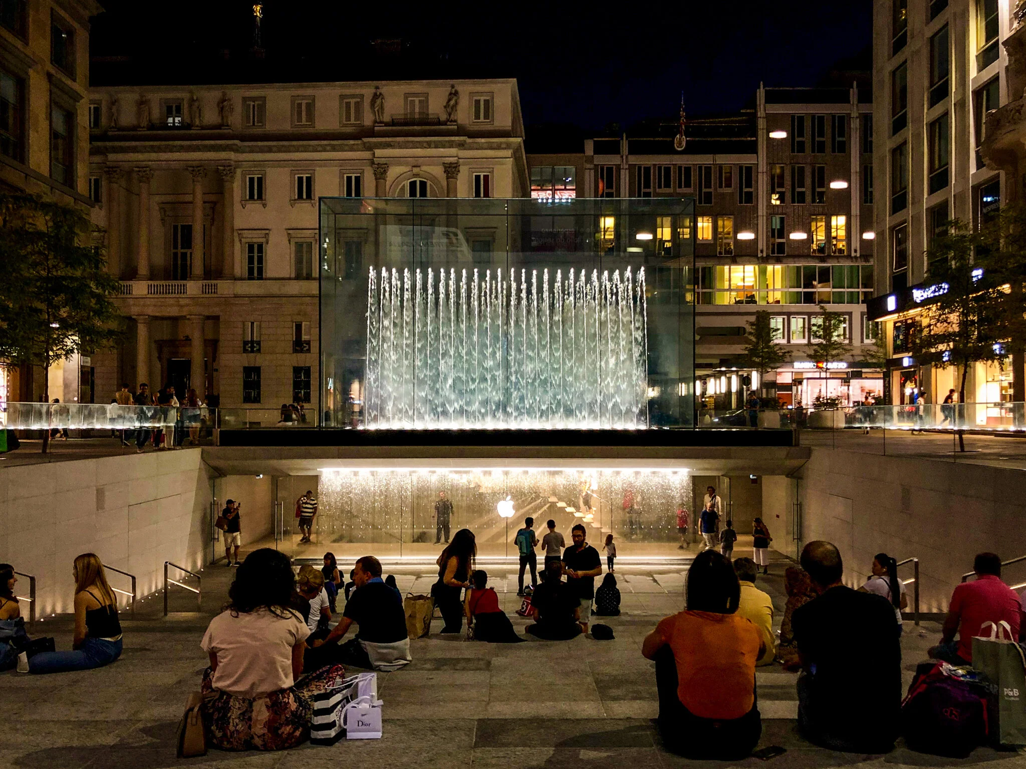  A glass-encased fountain crowns an underground Apple Store at the Piazza del Liberty in Milan.⁠ Below the fountain, water travels down to a glass wall that people stand behind while their friends and family members snap photos of them—presumably wit