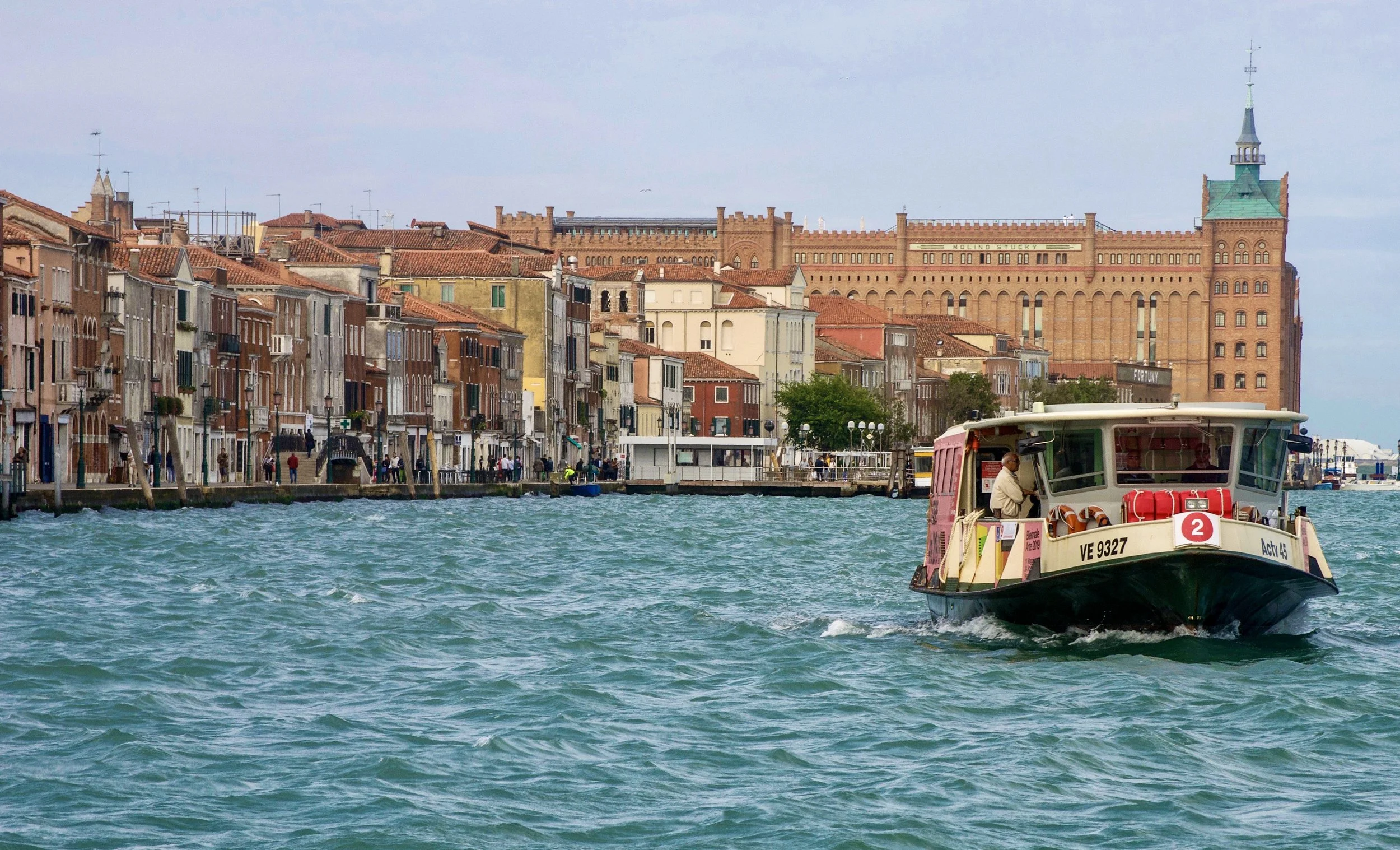  A taxi-boat cruises along the Giudecca canal in  Venice. The towering building in the distance is the neo-  Gothic Molino Stucky on Giudecca island. German architect  and artist Ernst Wullekopf designed the building, and Swiss  businessman Giovanni 