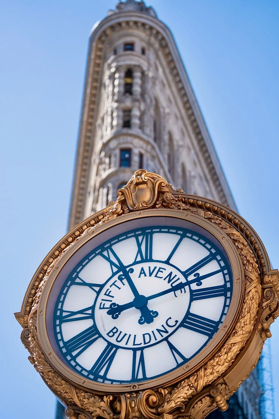  A fixture since 1909, the Fifth Avenue Clock stands 19 feet tall on the sidewalk at 200 Fifth Avenue in the Flatiron District. The double-faced, gilded cast-iron clock is the work of Brooklyn’s Hecla Iron Works. The clock sports an oak leaf wreath-f