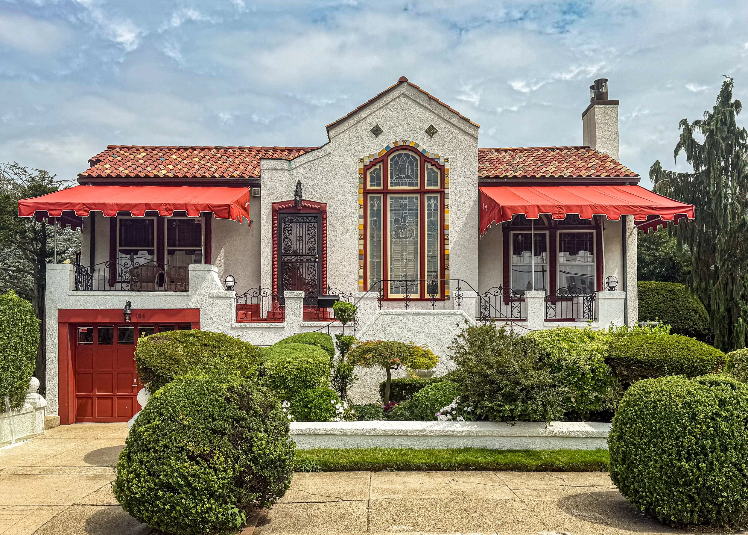   Built in 1932 in Long Beach, New York, this house looks like either Spanish Colonial Revival or Mediterranean Revival style, sporting a white stucco exterior, a large arched stained-glass window, wrought-iron railings, rich red canvas window awning
