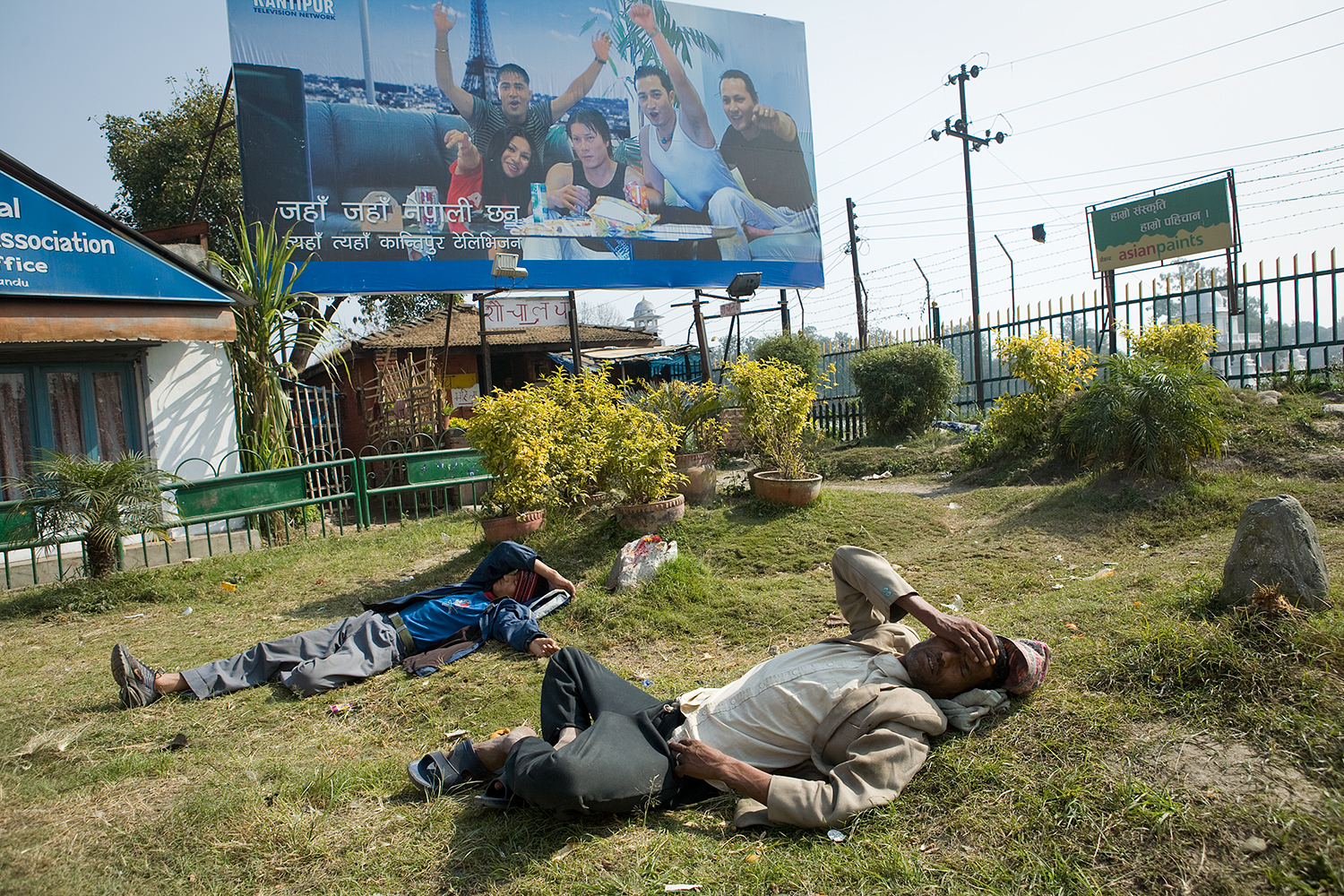 Two men lie in the grass near the intersection of busy streets in Kathmandu. 