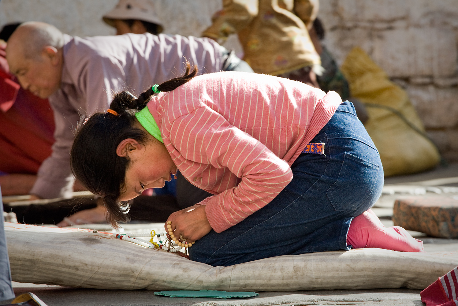  Engrossed in her mala, or prayer beads, a young pilgrim rests from her prostrating in front of the Jokhang temple in Lhasa. 