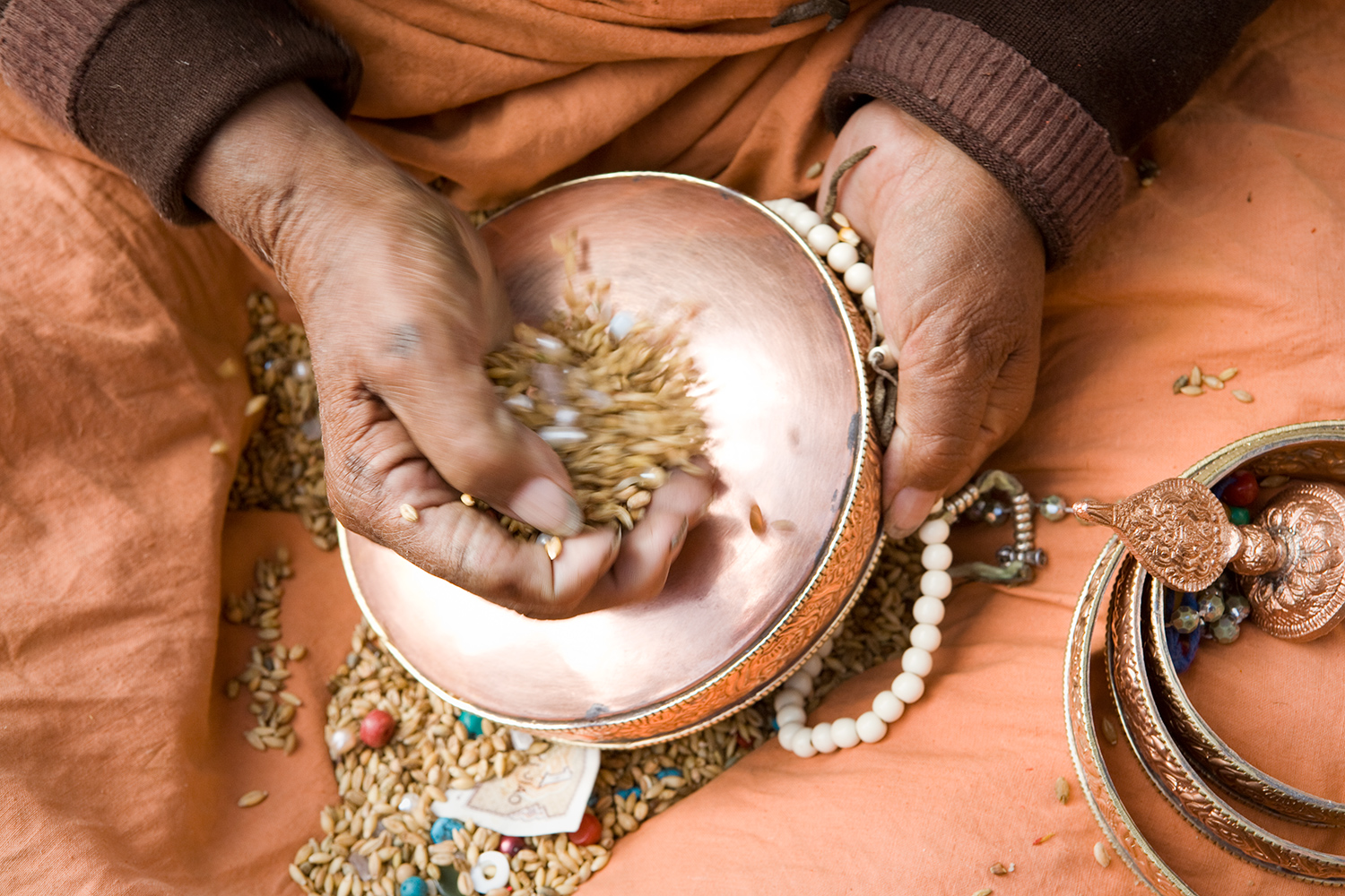  A woman hums a mantra while continuously pouring seeds and beads over a copper drum. 