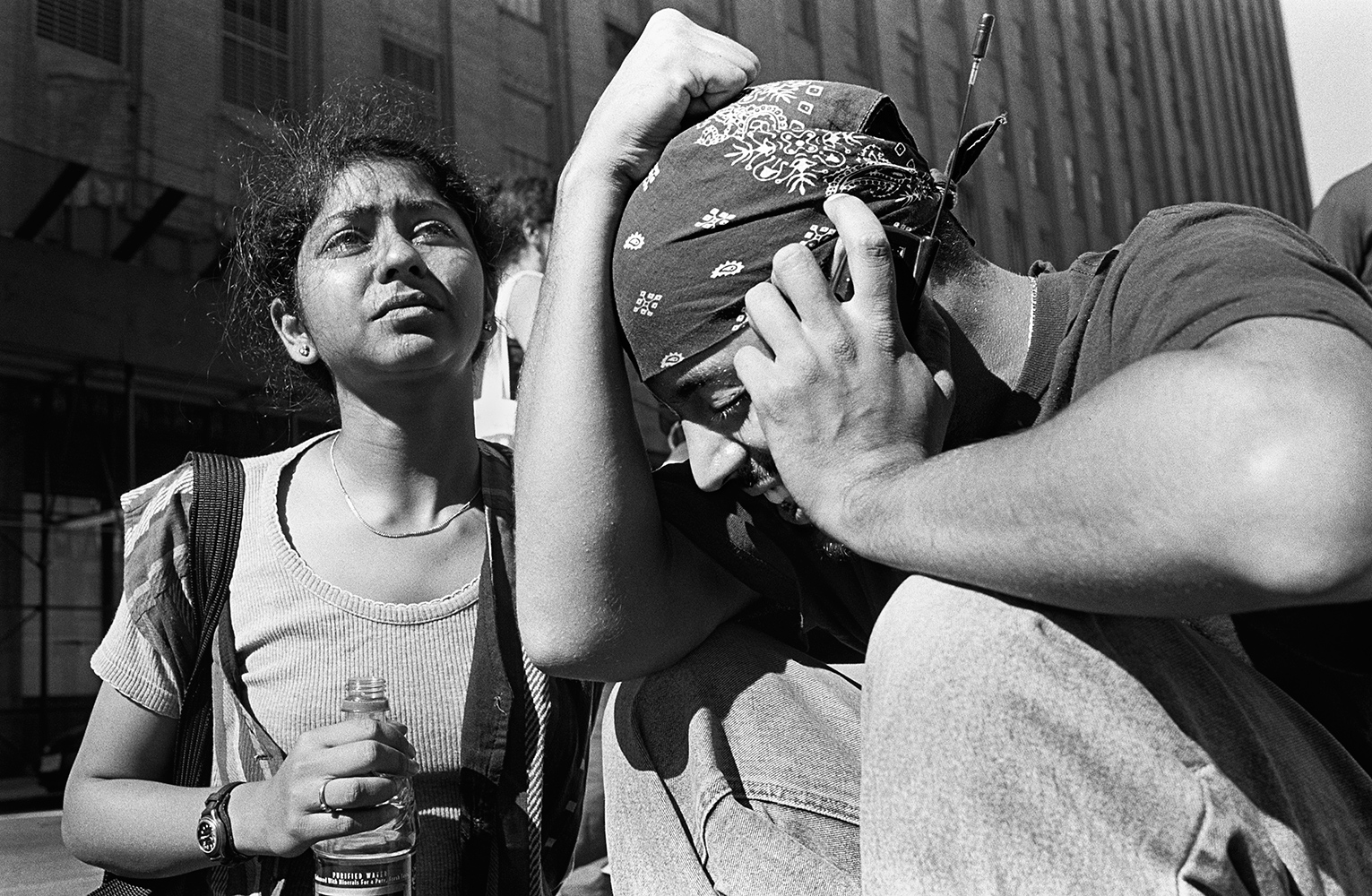  A man cries while talking to a family member on his cell phone. A stranger to him, the woman, left, tried to comfort him with water and by rubbing his neck. 