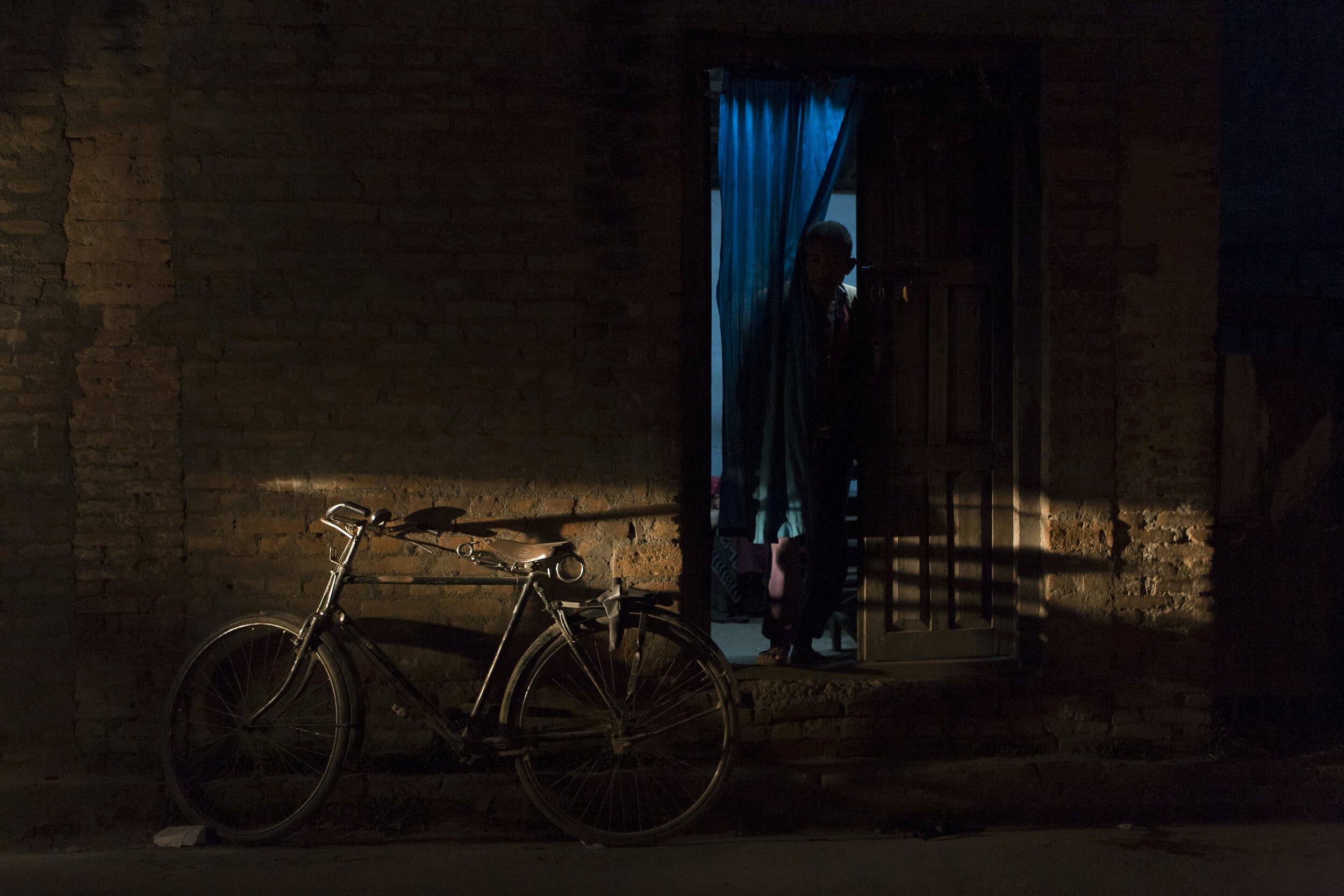  A man looks from his home as a motorcycle lights up a street in the exhaust-filled city of Kathmandu. 