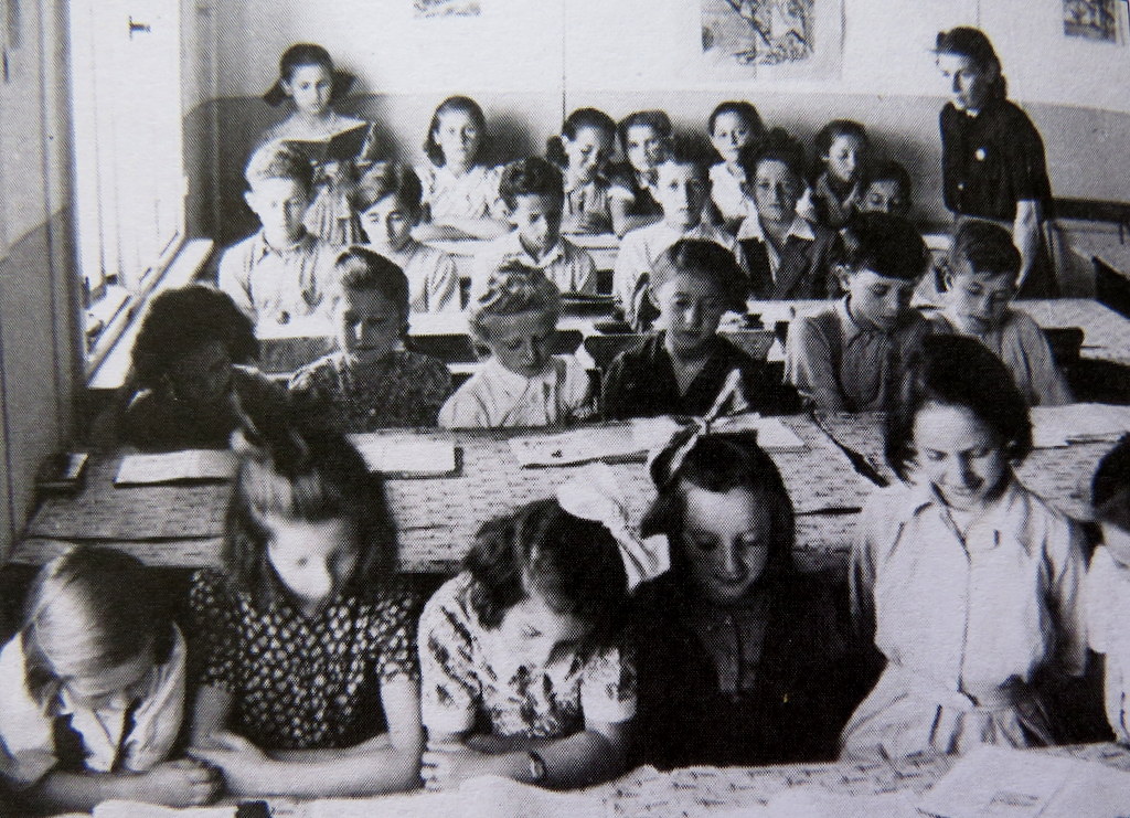 Judy standing, reading aloud to the class, back left corner, Schlachtensee DP camp, 1947