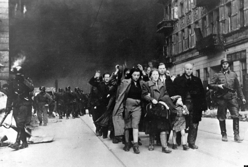 Warsaw Ghetto, May 1943. The sky is black with smoke from burning buildings while captured Jews are moved out for deportation.