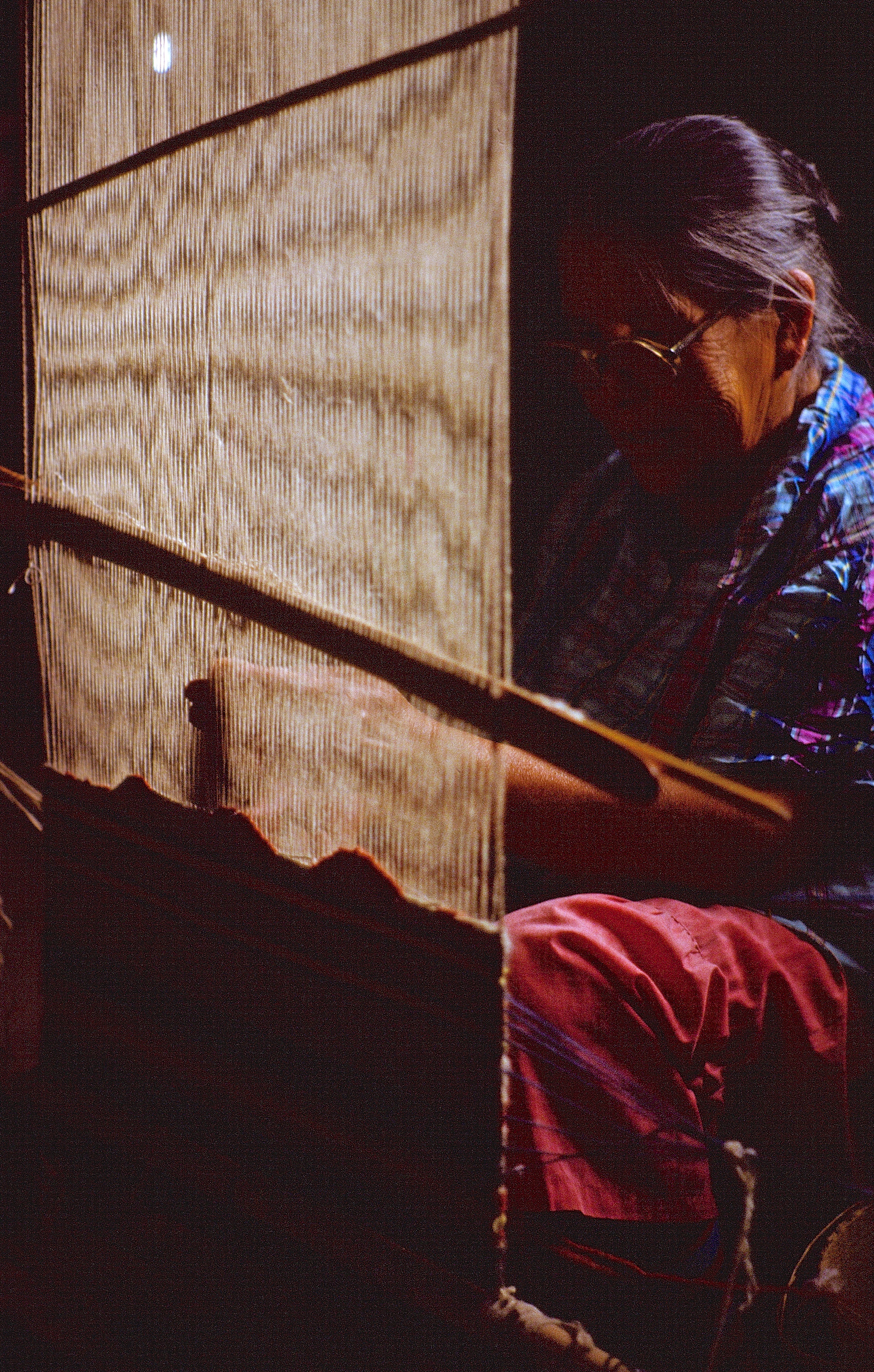 Mabel Woodman weaving by the light of a kerosine lamp and a wood stove (1984-85)