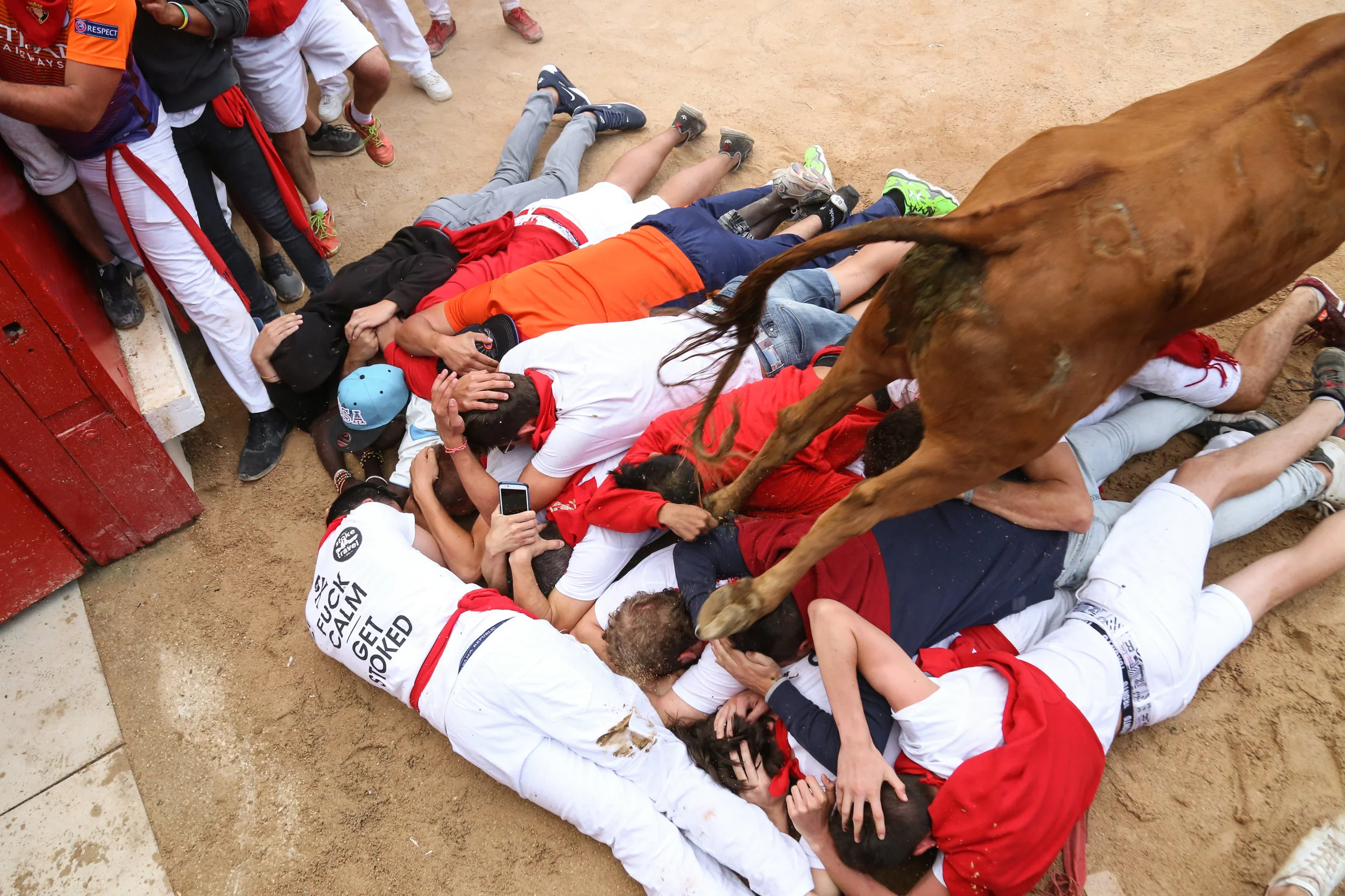 A calf jumps on top of people gathered in front of a door for 'the encierro de torros', in which young calves are let loose for mozos to try their luck at maneuvering around them. July 14th, 2017