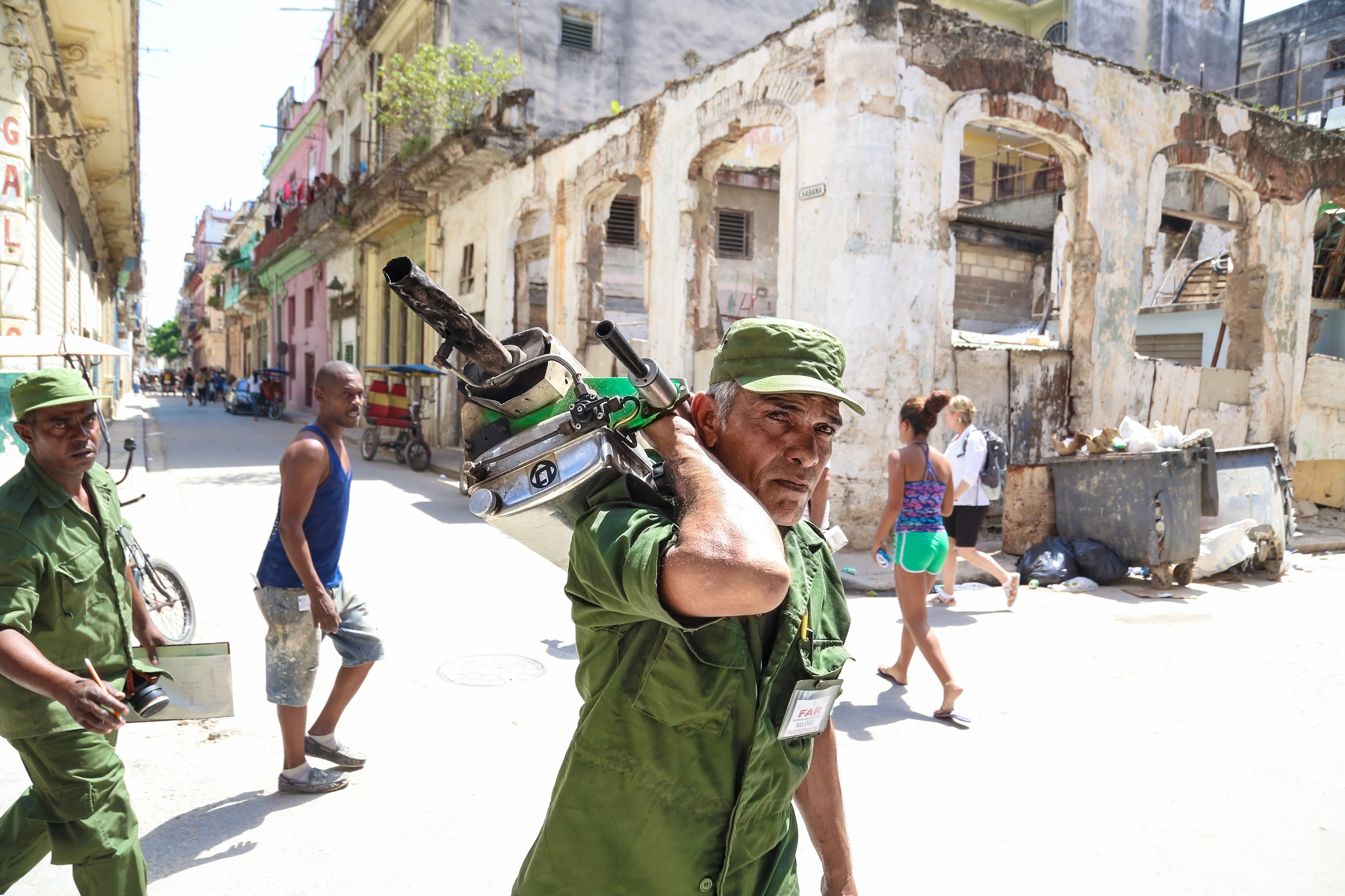 A member of the FAR (Fuerzas Armadas Revolucionarias / Revolutionary Armed Forces) walks around the streets of Havana with his makeshift fumigation machine followed by another member of the FAR keeping track of the homes and businesses already fumigated. March 31st, 2016.
