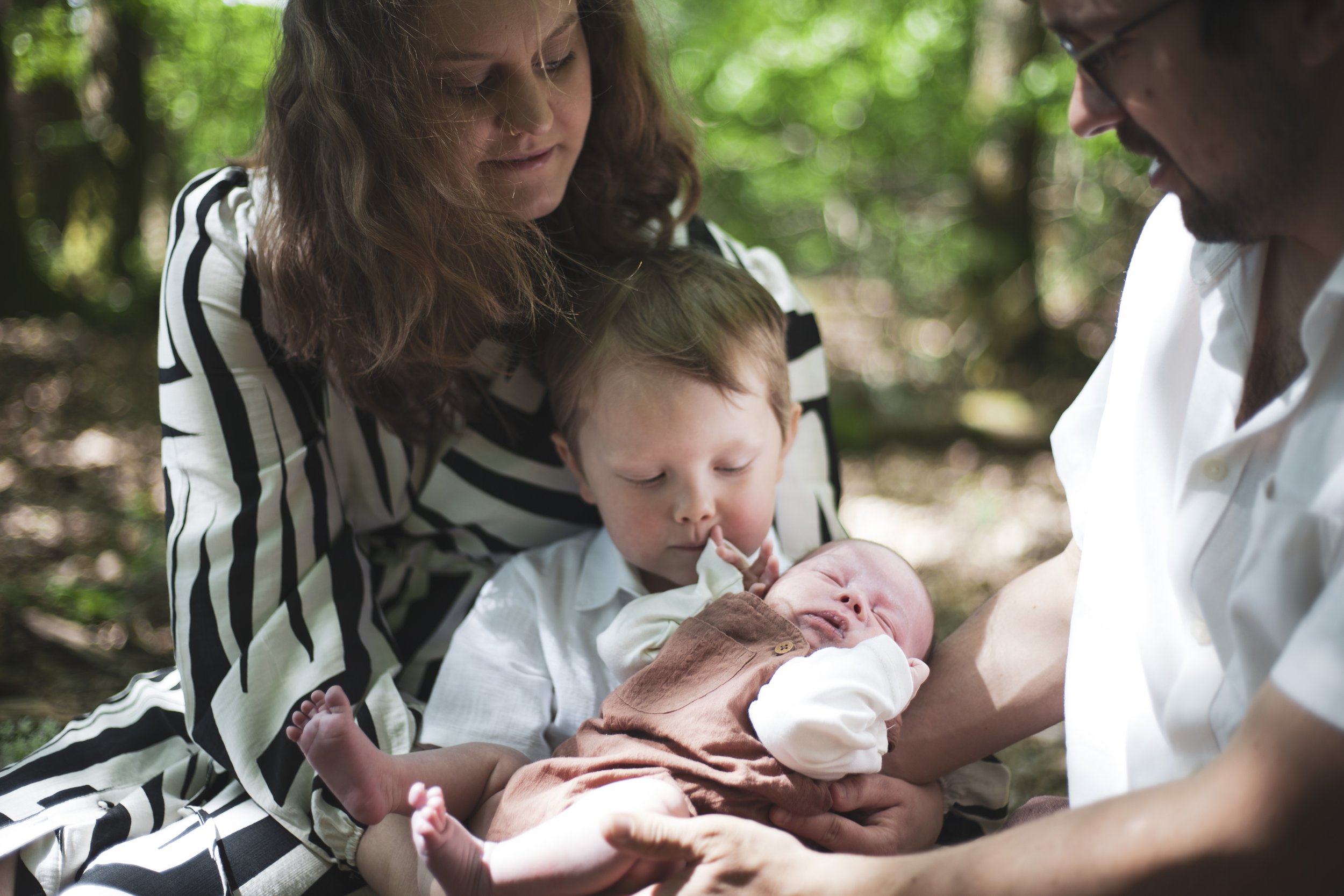 Eine Familie im Wald, mit einem Baby in den Armen, das in einer Hebammen- oder Geburtszeremonie gehalten wird. Familienportrait, Saarland, Wadern. 