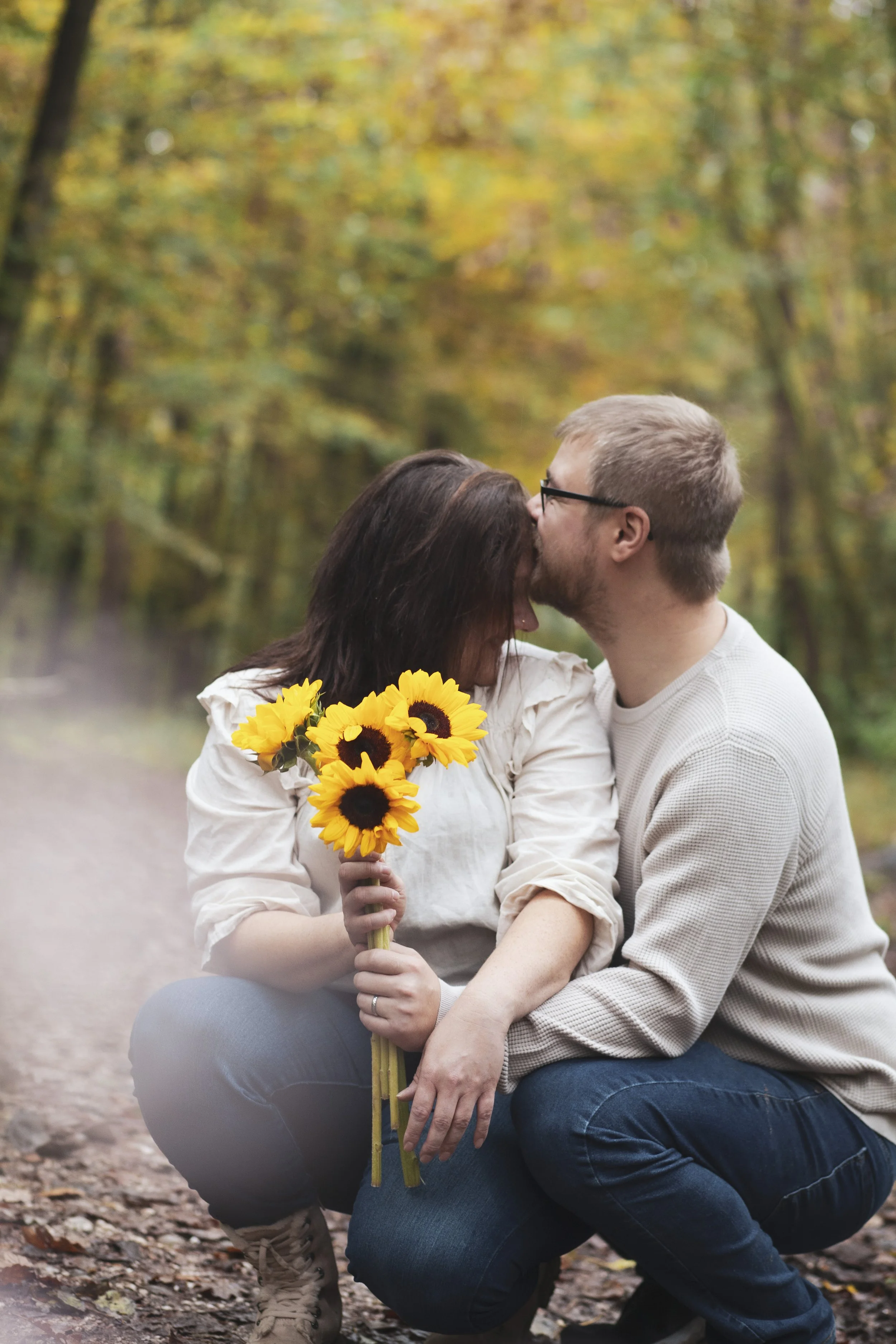 Ein Paar umarmt sich in einem Park im Herbst, die Frau hält einen Strauss Sonnenblumen, im Hintergrund sind bunte Herbstbäume.