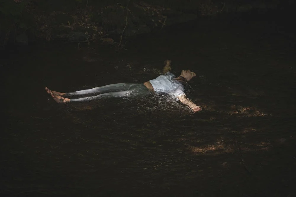 Frau liegt auf dem Rücken im dunklen Wasser in der Nacht, mit ausgestreckten Armen und geschlossenen Augen.