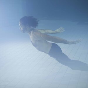 Eine Person, die unter Wasser im Schwimmbecken liegt, seitlich mit den Armen ausgestreckt.