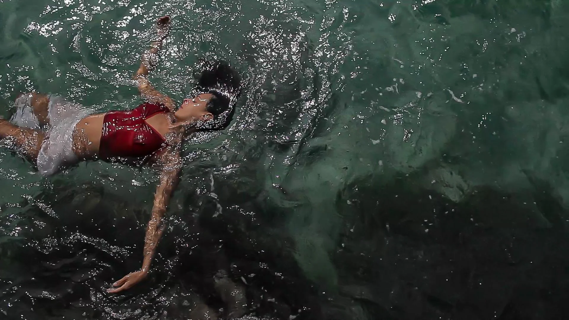 Ein Junge schwimmt im Wasser, trägt eine rote Jacke und eine Schwimmbrille.