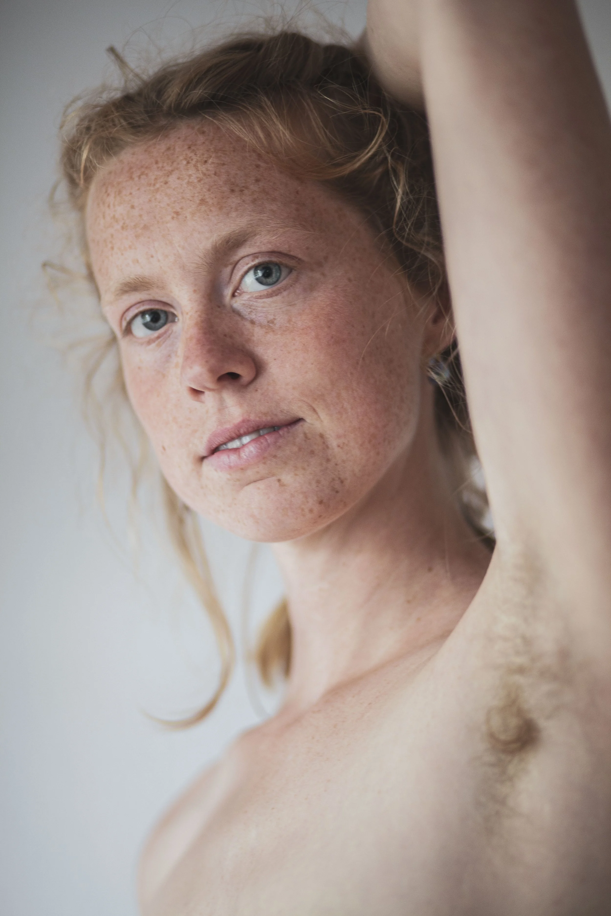 Nahaufnahme eines Frauengesicht mit roten Haaren, Sommersprossen und blauen Augen, die die Schulter berührt.
