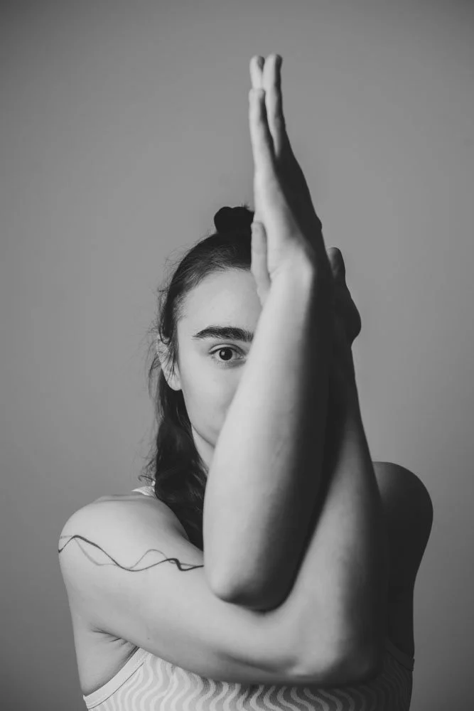 Schwarz-Weiß-Fotografie eines jungen mädchens mit einem Halbprofil, das seine Arme kreuzt und vor dem Gesicht hält, die linke Seite des Gesichts ist sichtbar, der Hintergrund ist grau.